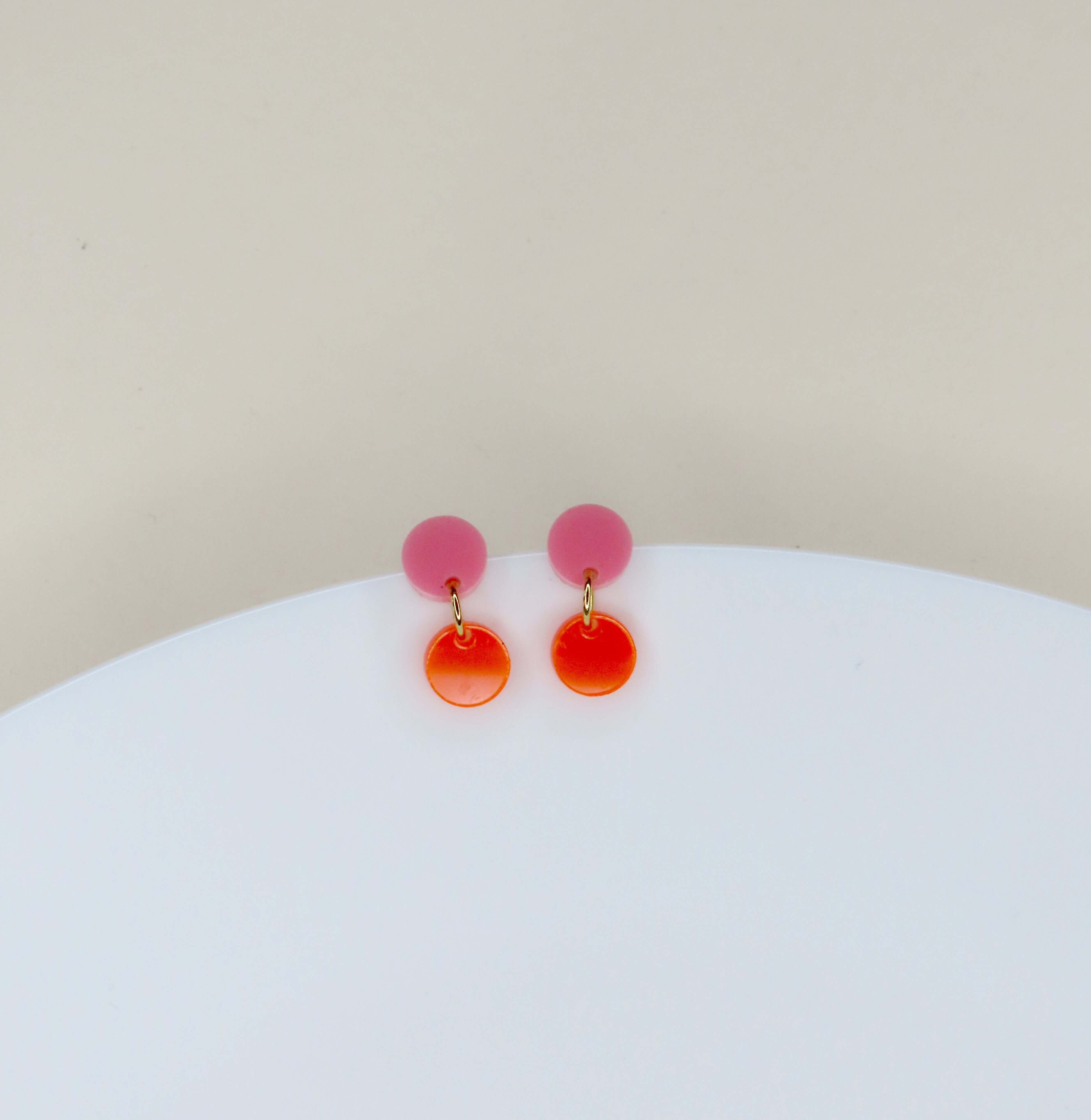 zarte rosa acryl-stecker in kreisform mit abgesetztem neonorange-hänger und goldenem verbindungselement