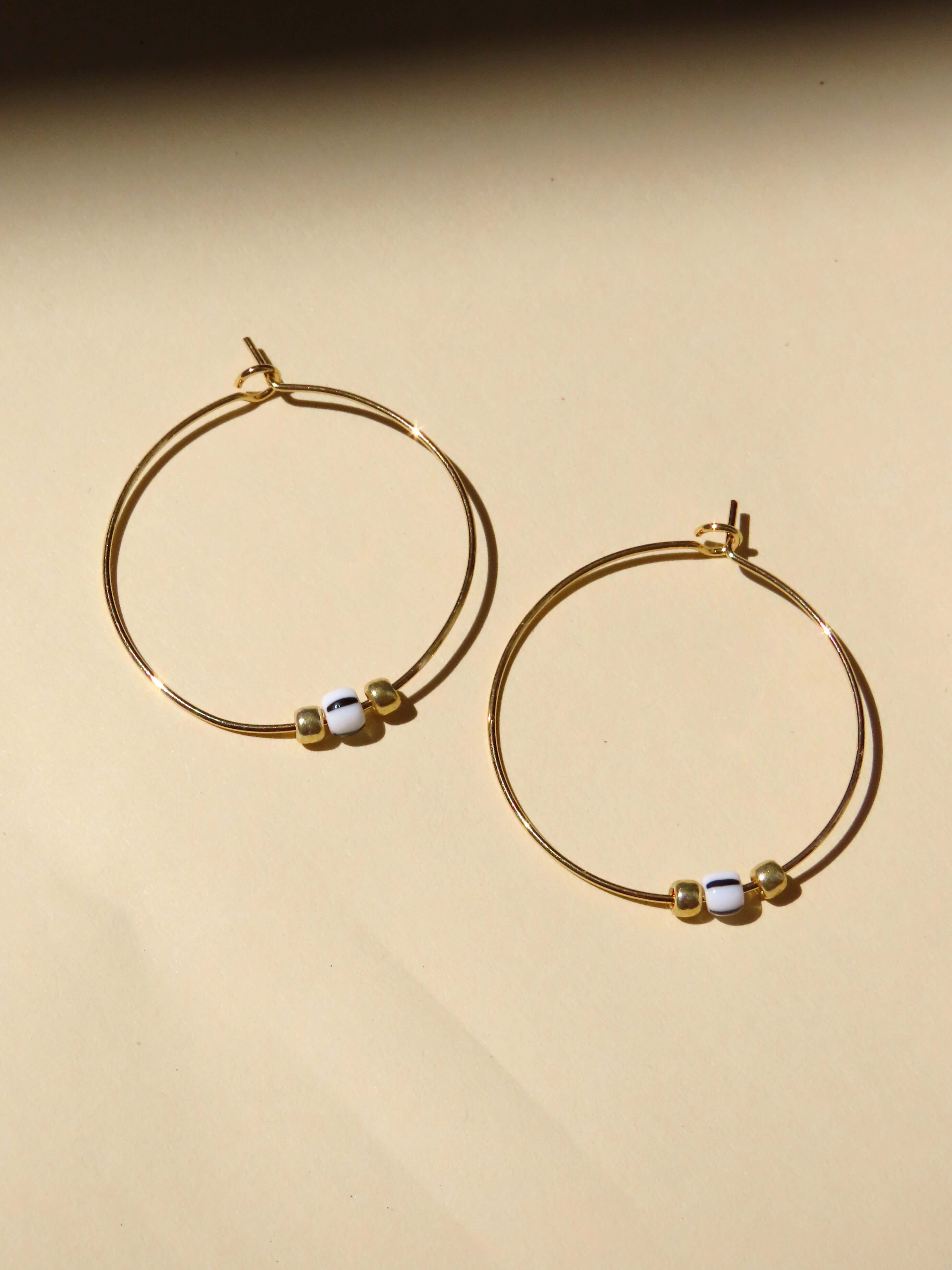 Kleiner goldener Kreisohrring aus Edelstahl Ø 3 cm, mit mittiger Glasperle in Schwarz-Weiß-Streifen und zwei goldenen Minikugeln