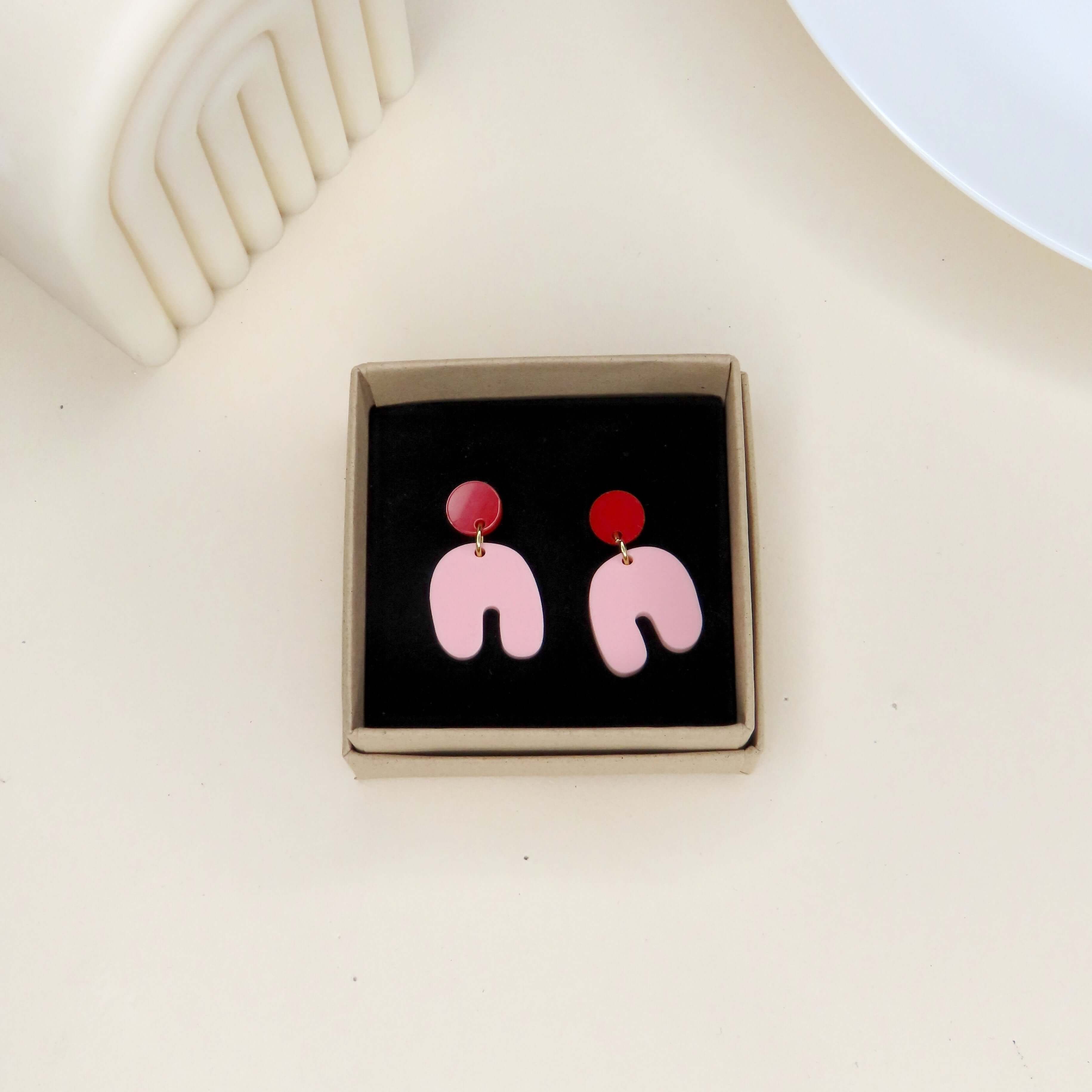 Geometrische Ohrringe in Rot und Rosa, bestehend aus rundem Kreisstecker und verspieltem Bogenanhänger