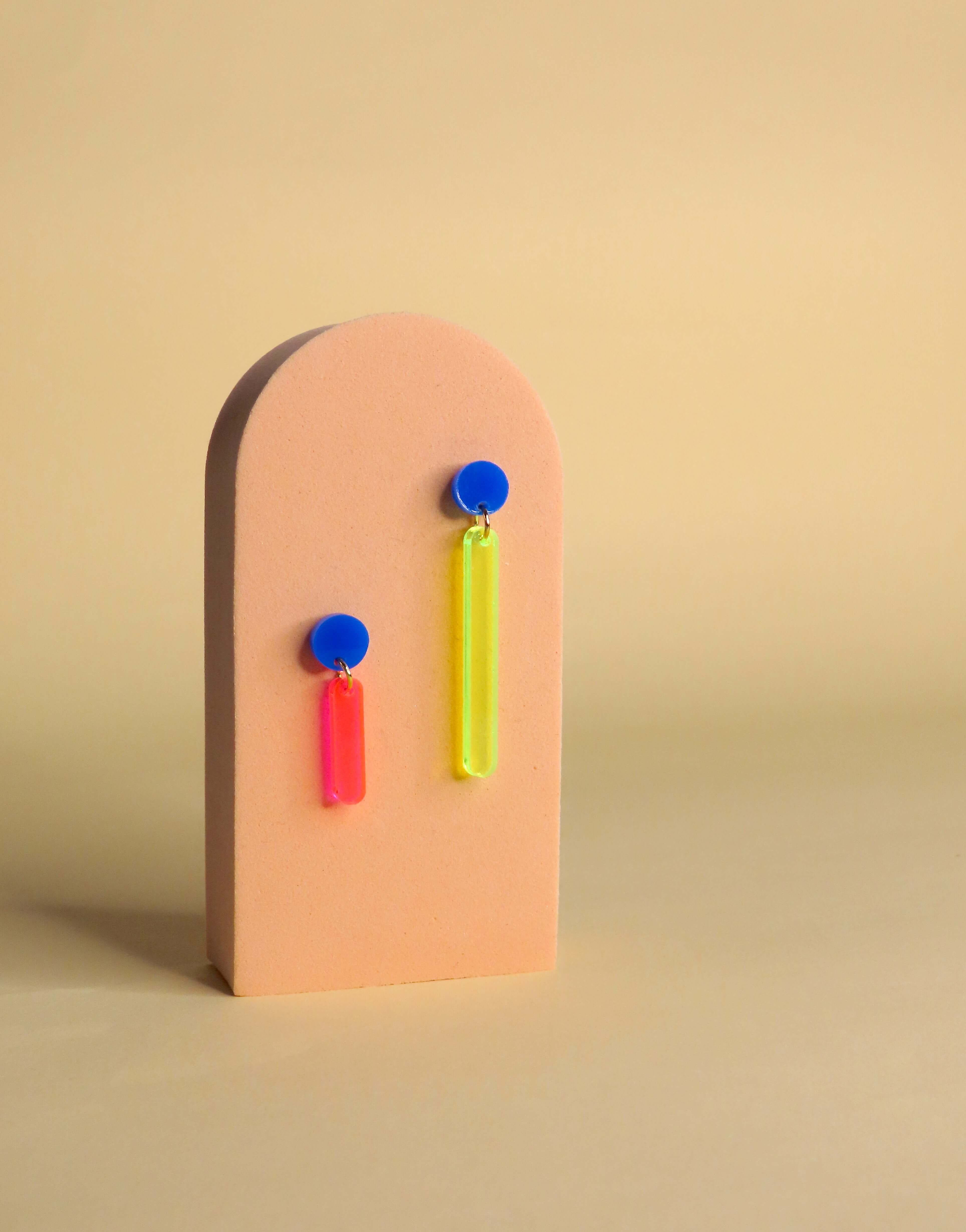 Auffällige Acryl-Ohrringe in asymmetrischer Form mit Neonpinkem und Neongelbem Anhänger an blauen Edelstahlsteckern