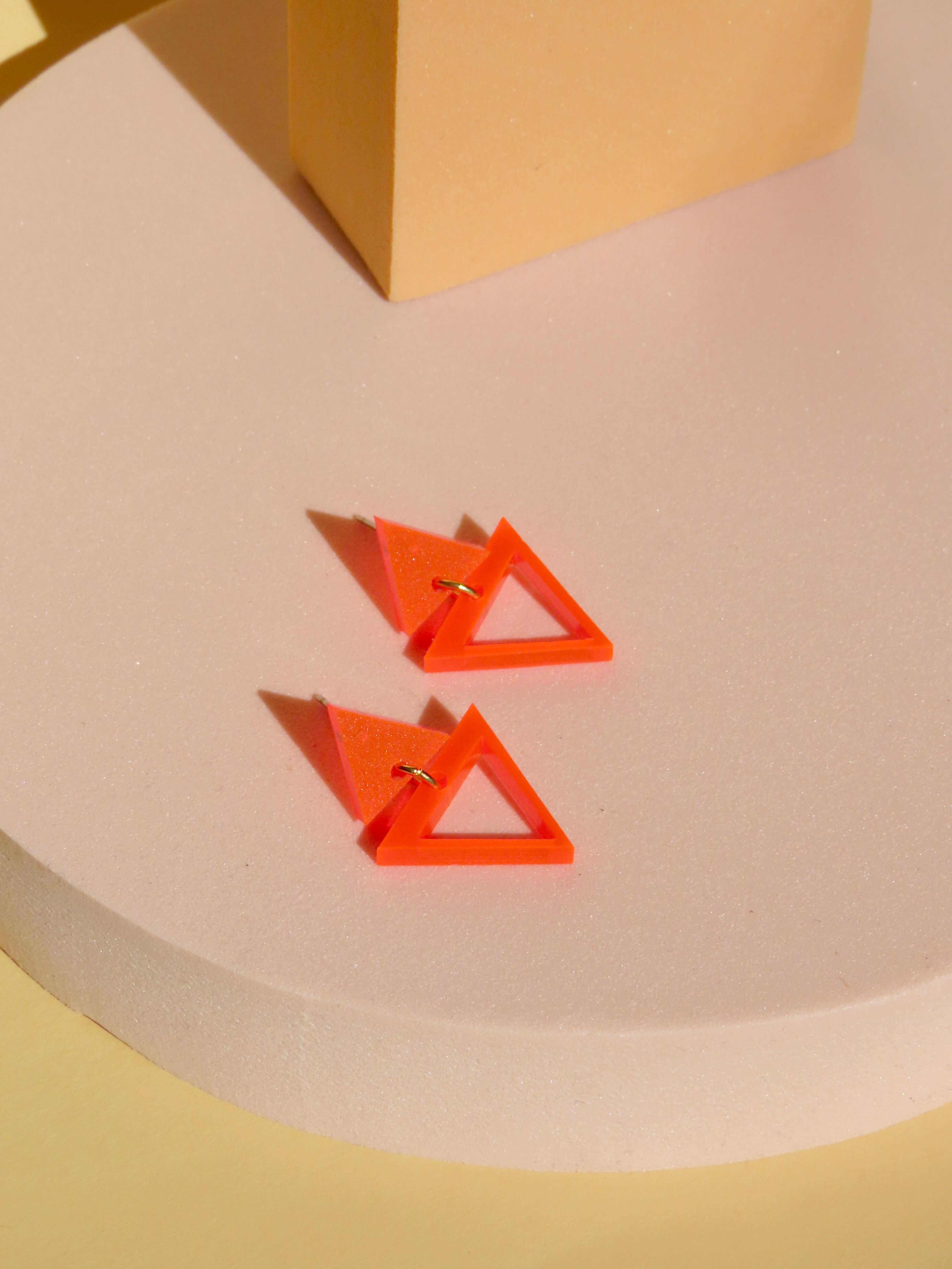 geometrische ohrhänger aus neonorangefarbenem acryl mit kleinem und großem dreieck, verbunden durch goldenes element