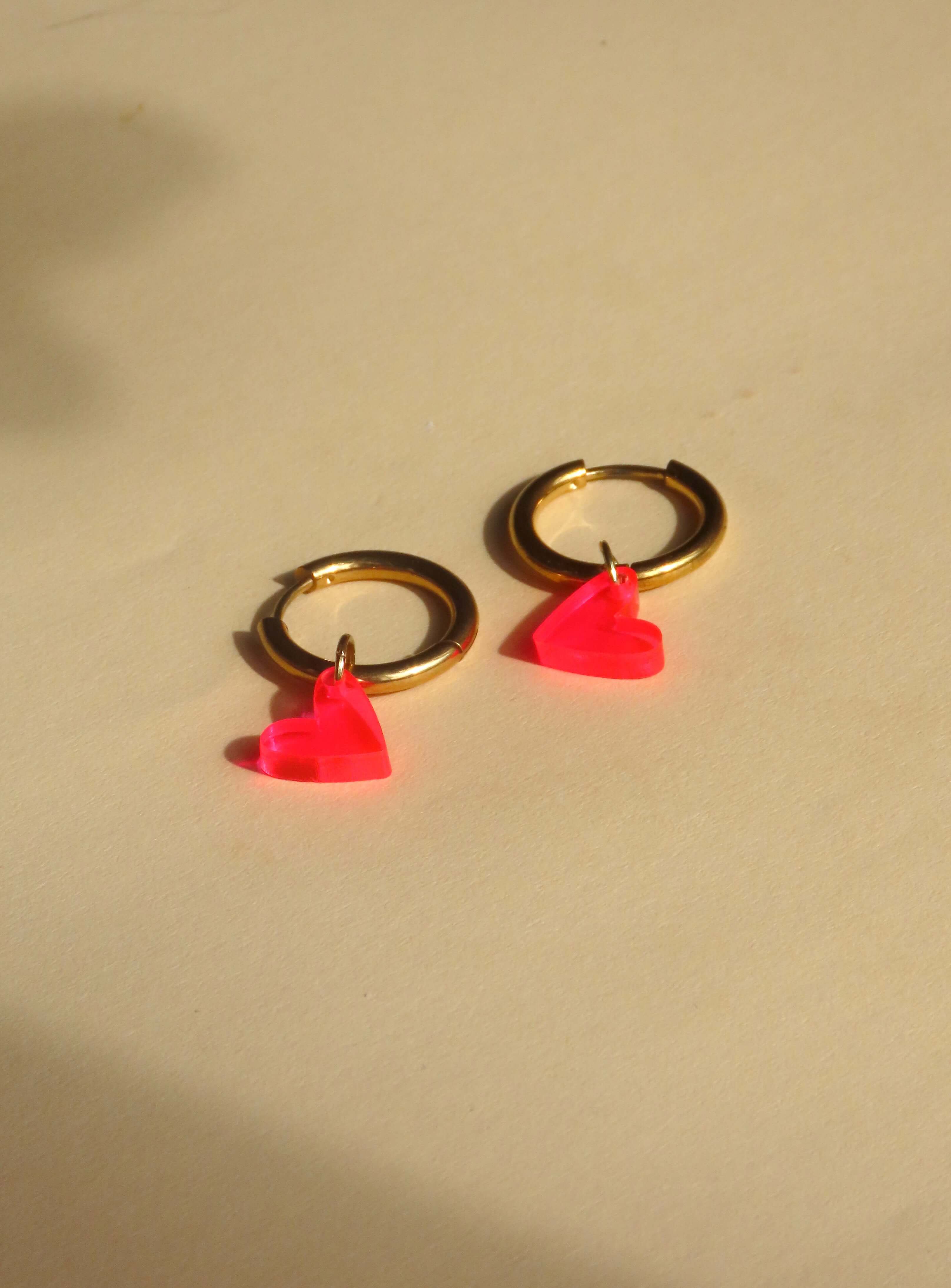 Verspielte Creolen mit transparenten Herzanhängern in Neon Pink und goldglänzendem Edelstahl