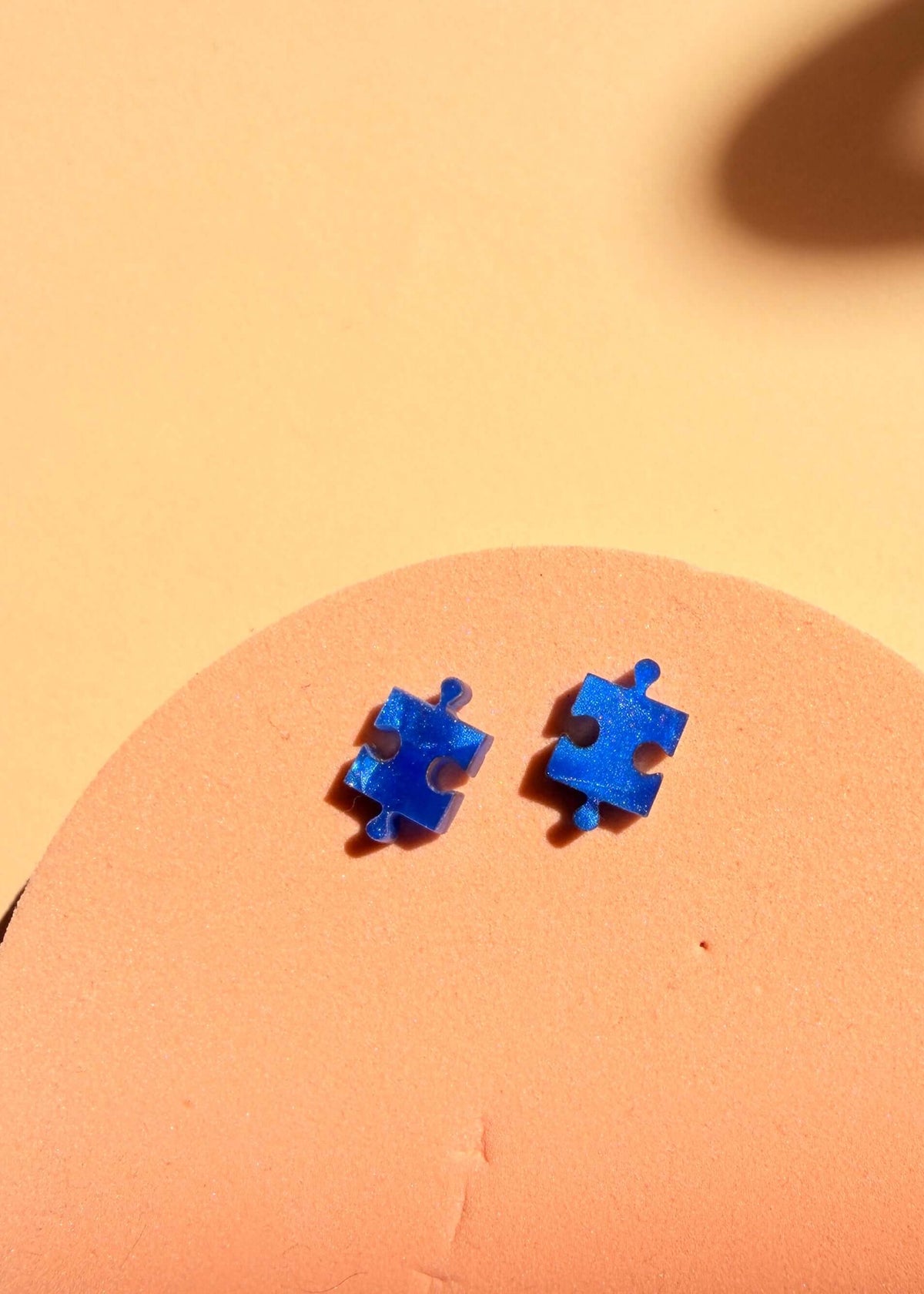 Ozeanblaue Puzzle Ohrstecker aus Edelstahl und Acryl – Detailansicht des Paares auf warmem Hintergrund