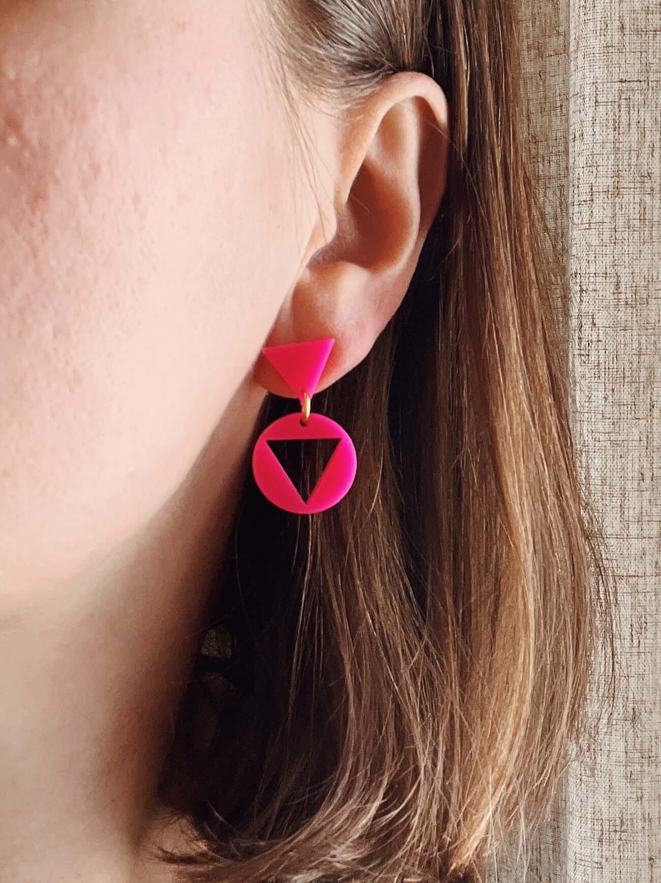 Leuchtend pinke Acryl Ohrhänger mit rundem Anhänger und ausgeschnittenem Dreieck, klar geometrische Form und glänzende Oberfläche.