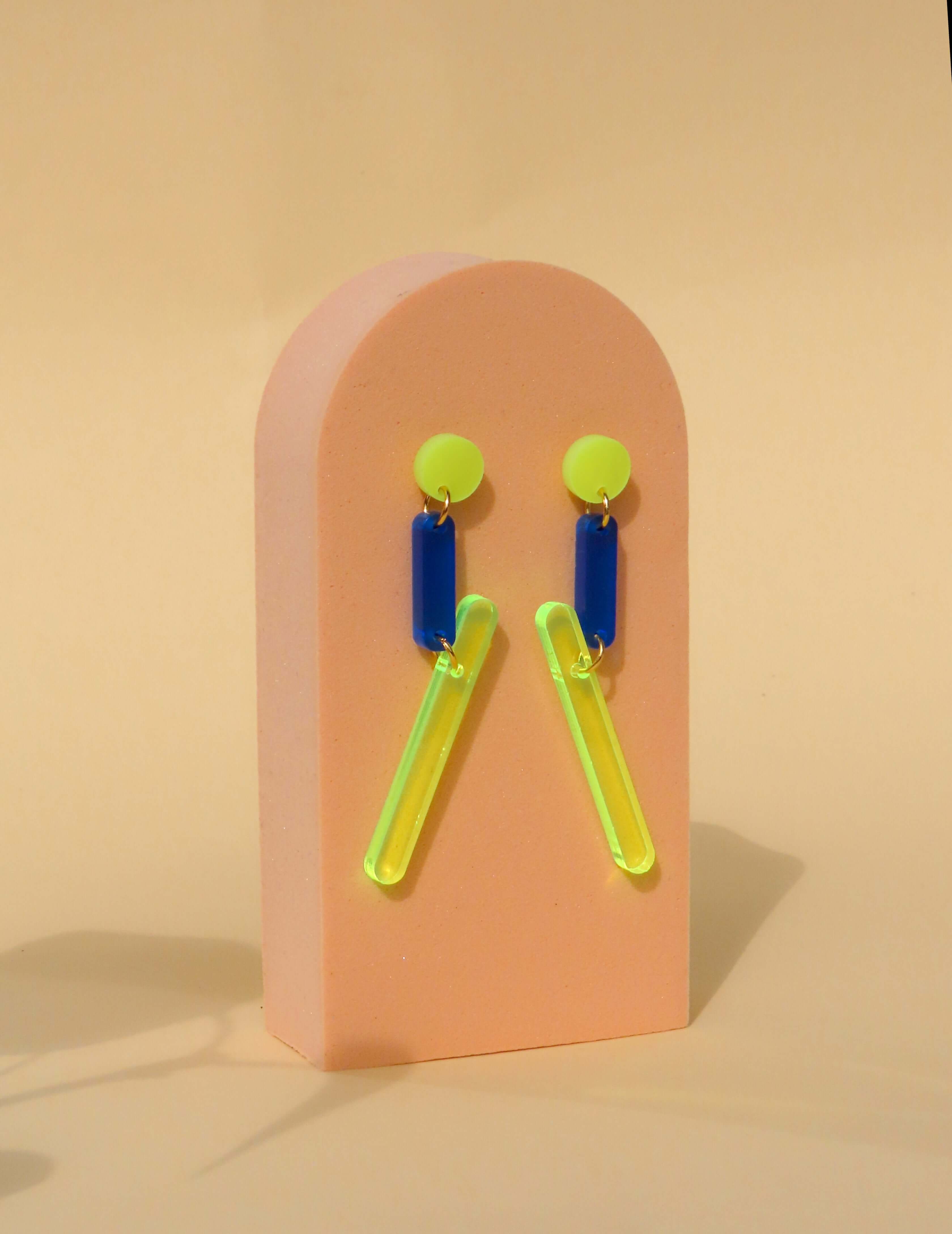 Neon-Design Ohrring aus Acryl: runder Stecker in Gelb, Verbindungsteil in Blau, daran hängender länglicher gelber Streifen