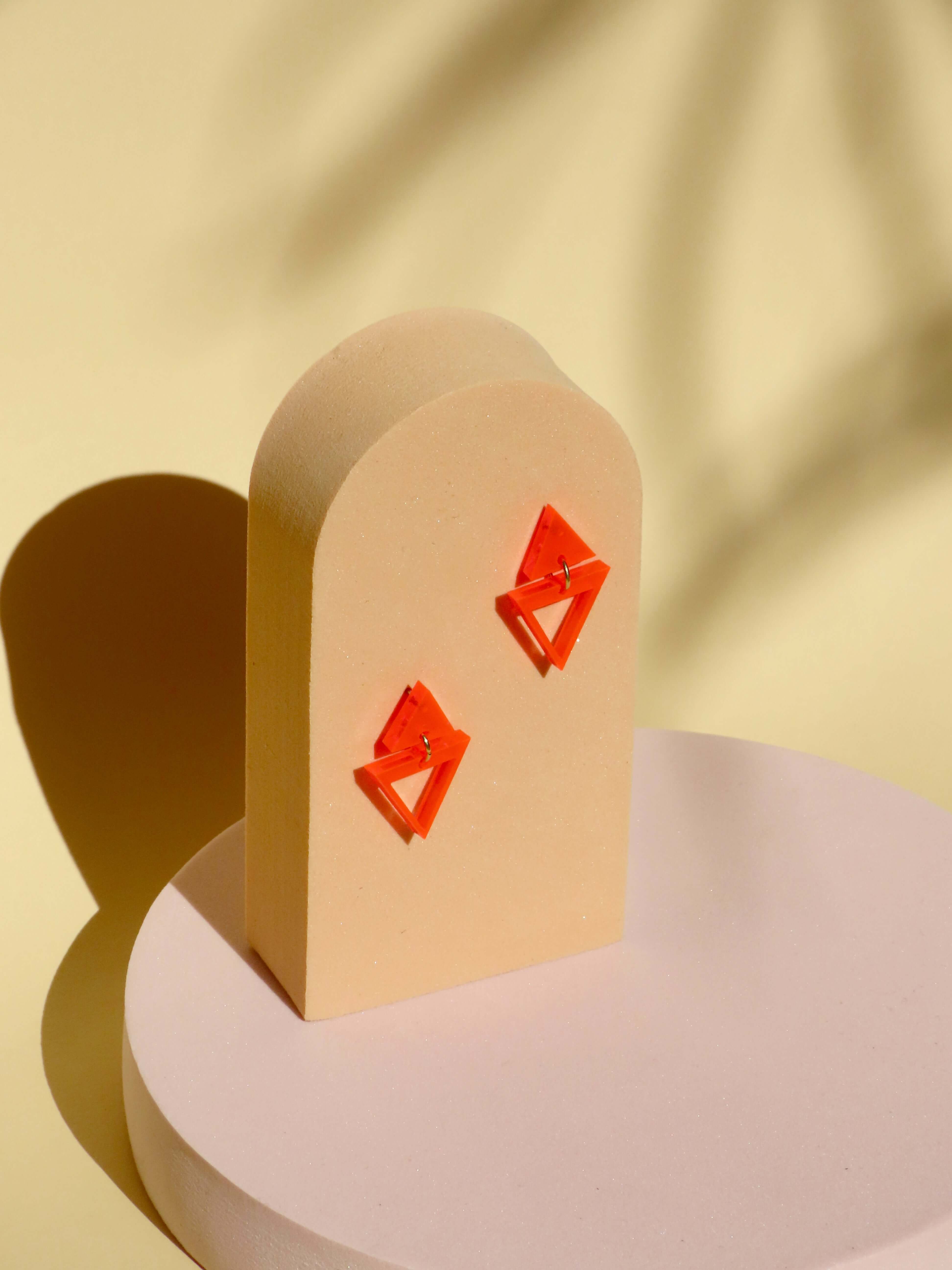leuchtend orange acryl ohrhänger mit zwei ineinandergreifenden dreiecken und glänzender transparenter oberfläche