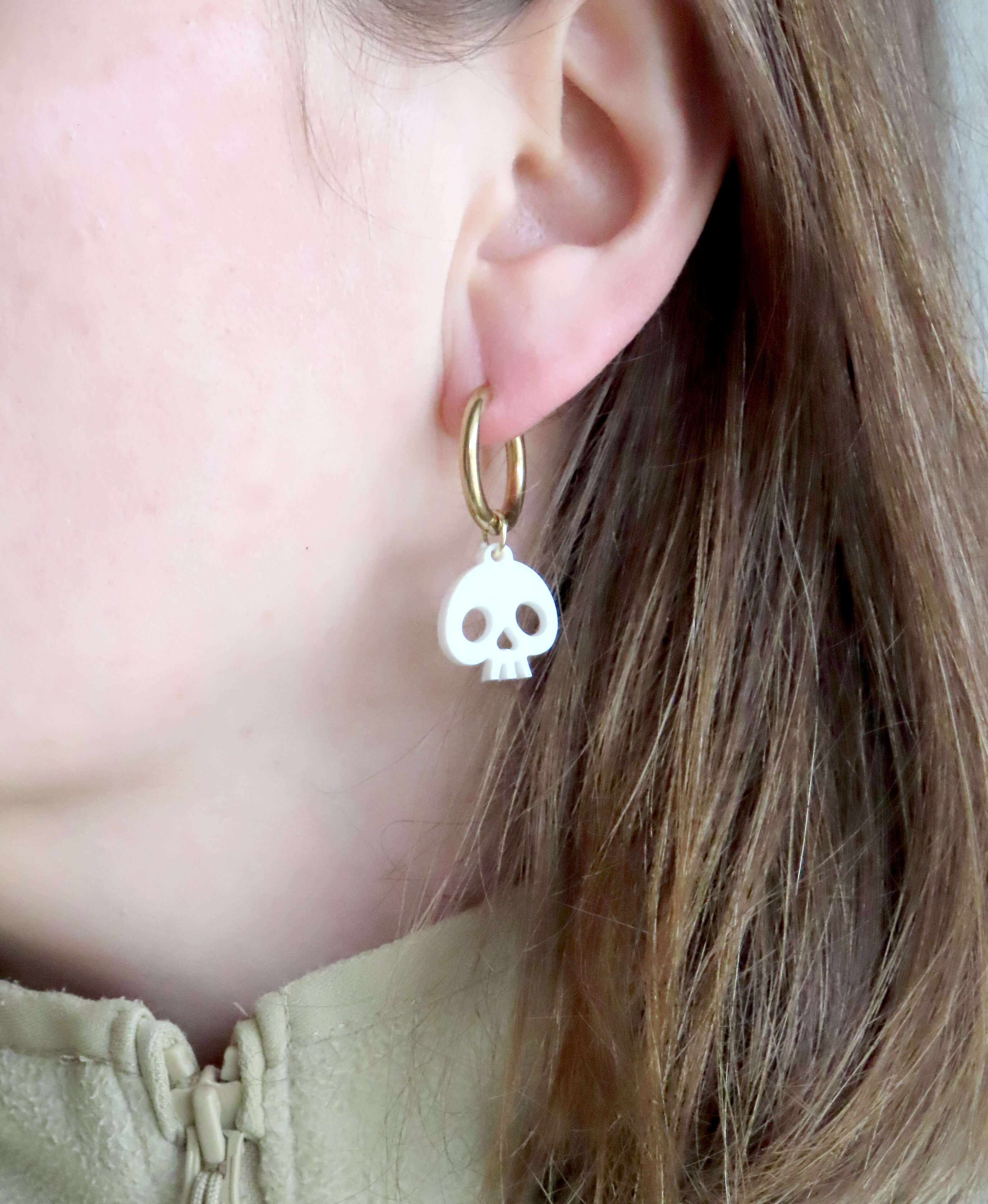 vergoldete Edelstahl-Creolen mit schwingenden weißen Totenkopf-Elementen aus Acryl, klarer Kontrast von Gold und Weiß