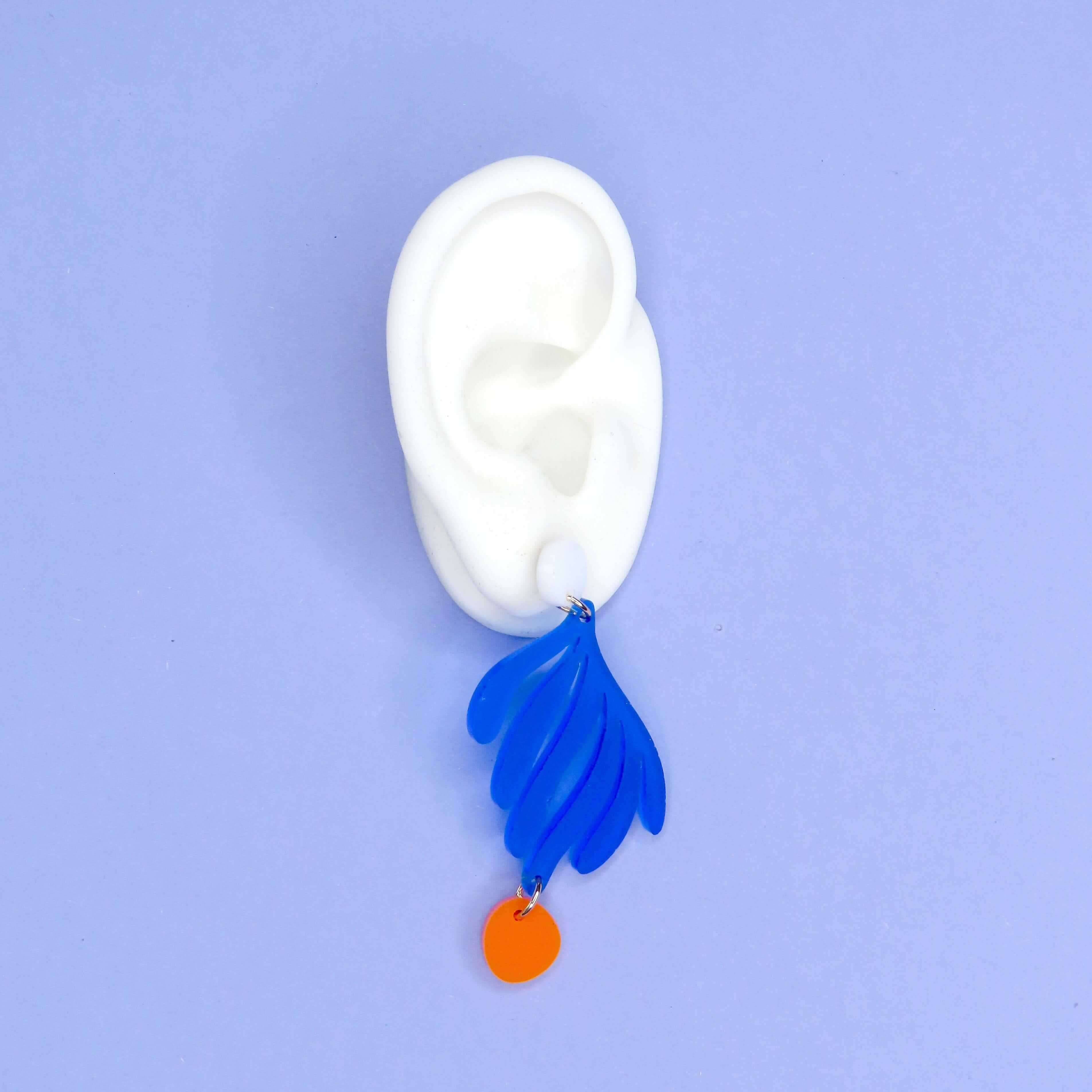 Kunstvolle Ohrringe aus Acryl in kräftigem Blau mit orangefarbenem runden Anhänger in blattähnlichem Design