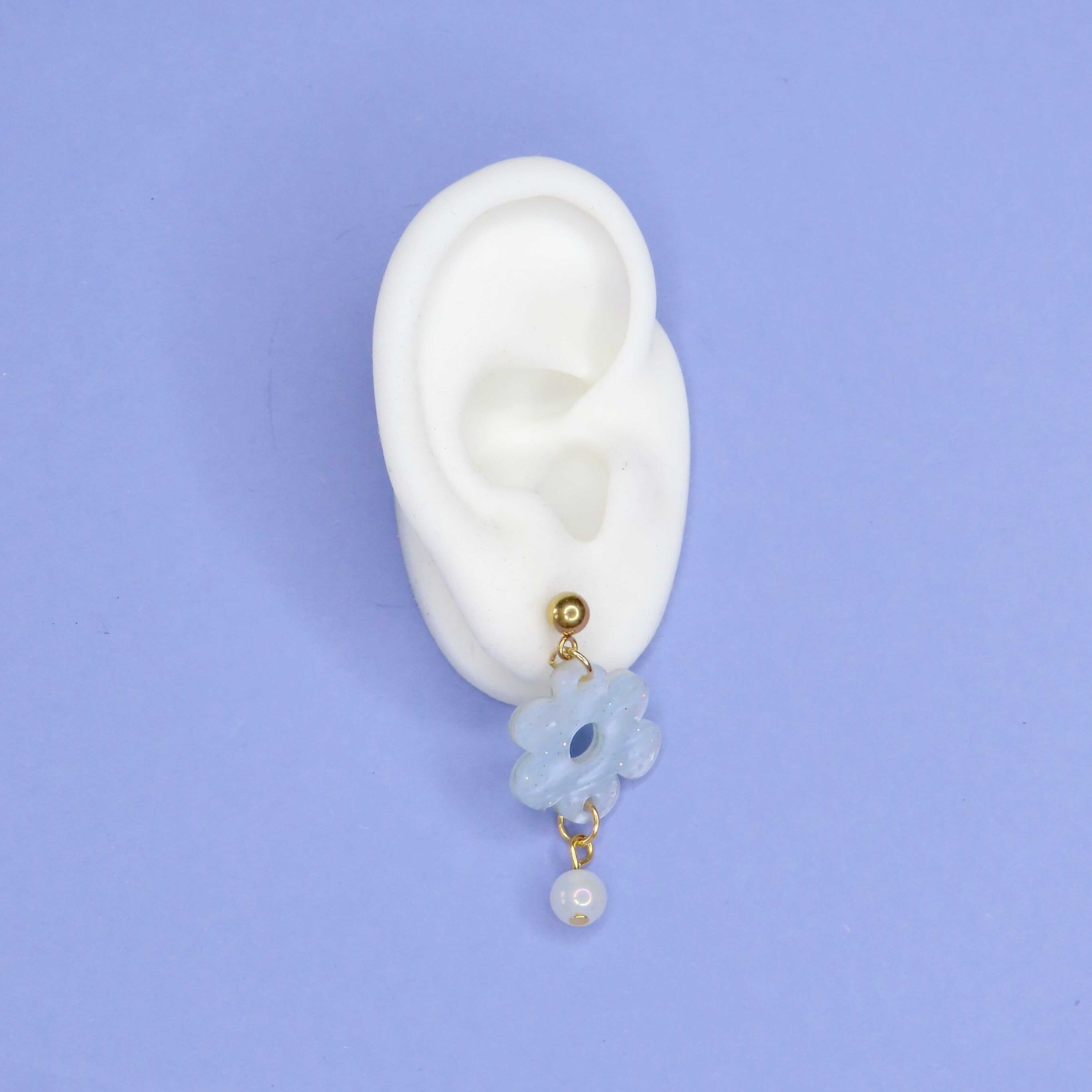 Blumenförmige Acryl-Ohrringe in sanftem Eisblau mit goldenem Stecker und hängender weißer Perle als Akzent