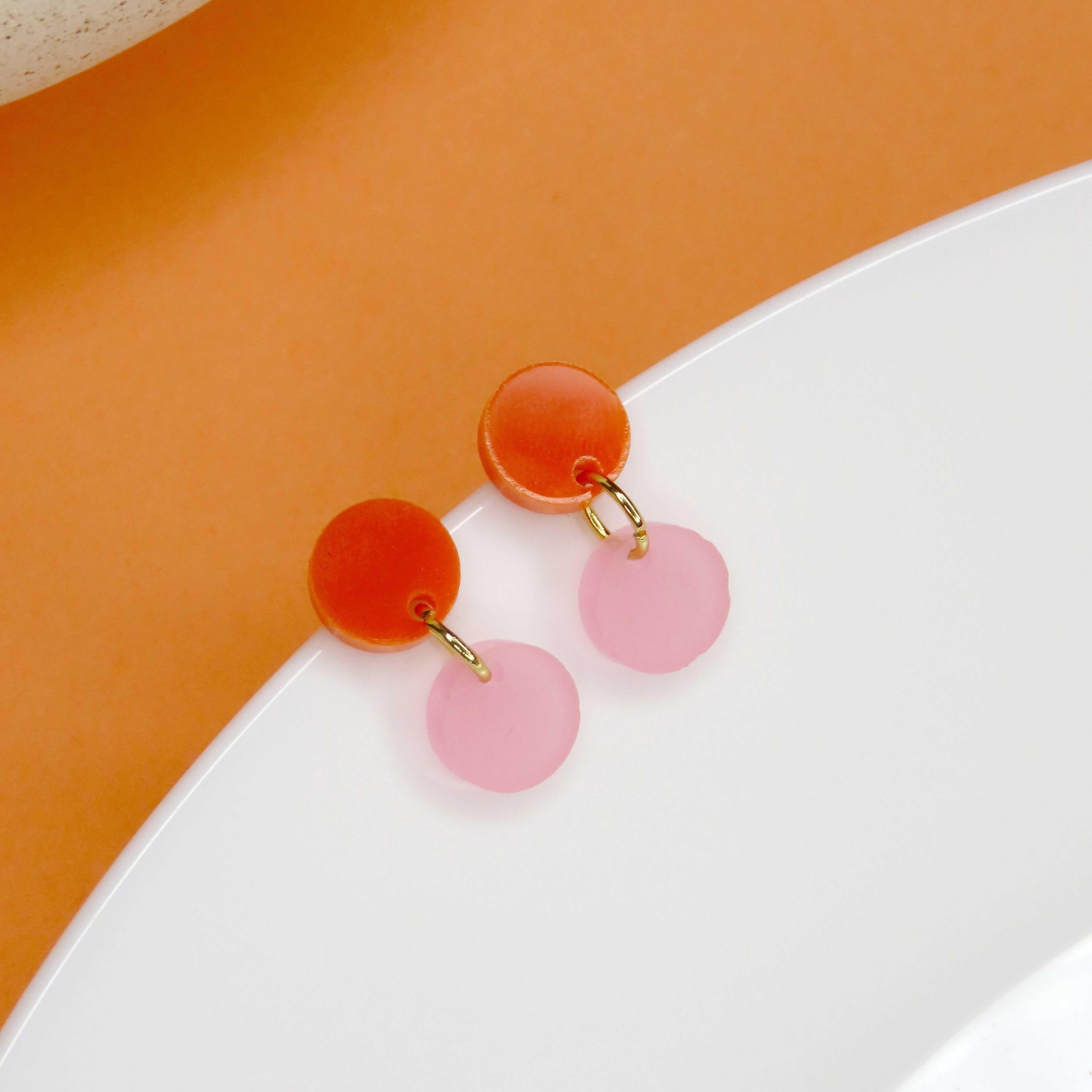 Runde Ohrstecker mit glänzendem orangefarbenem Element und zartem rosa Anhänger