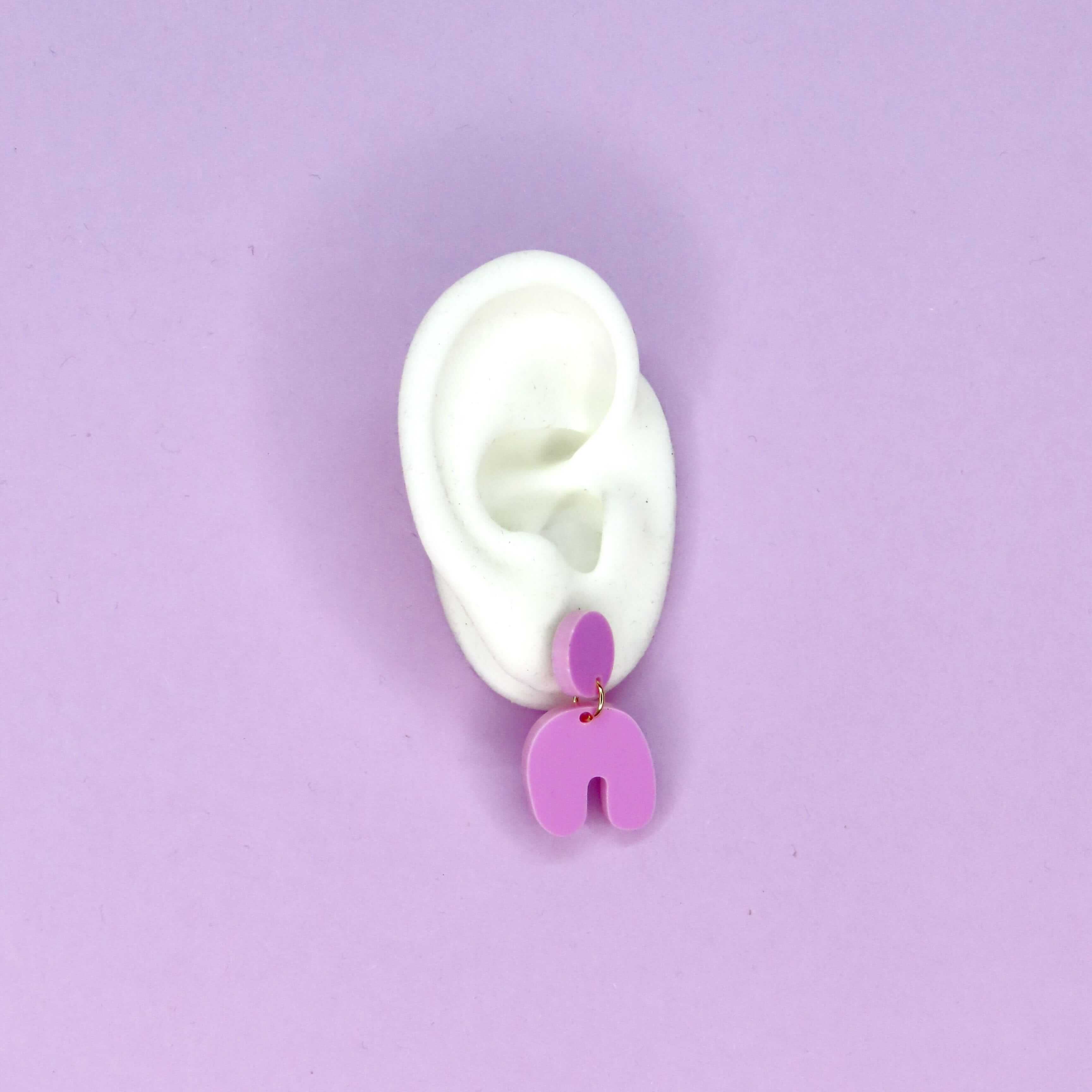 Paar hängender Acrylohrringe in mattem Himbeerrosa mit rundem Stecker und bogenförmigem Anhänger