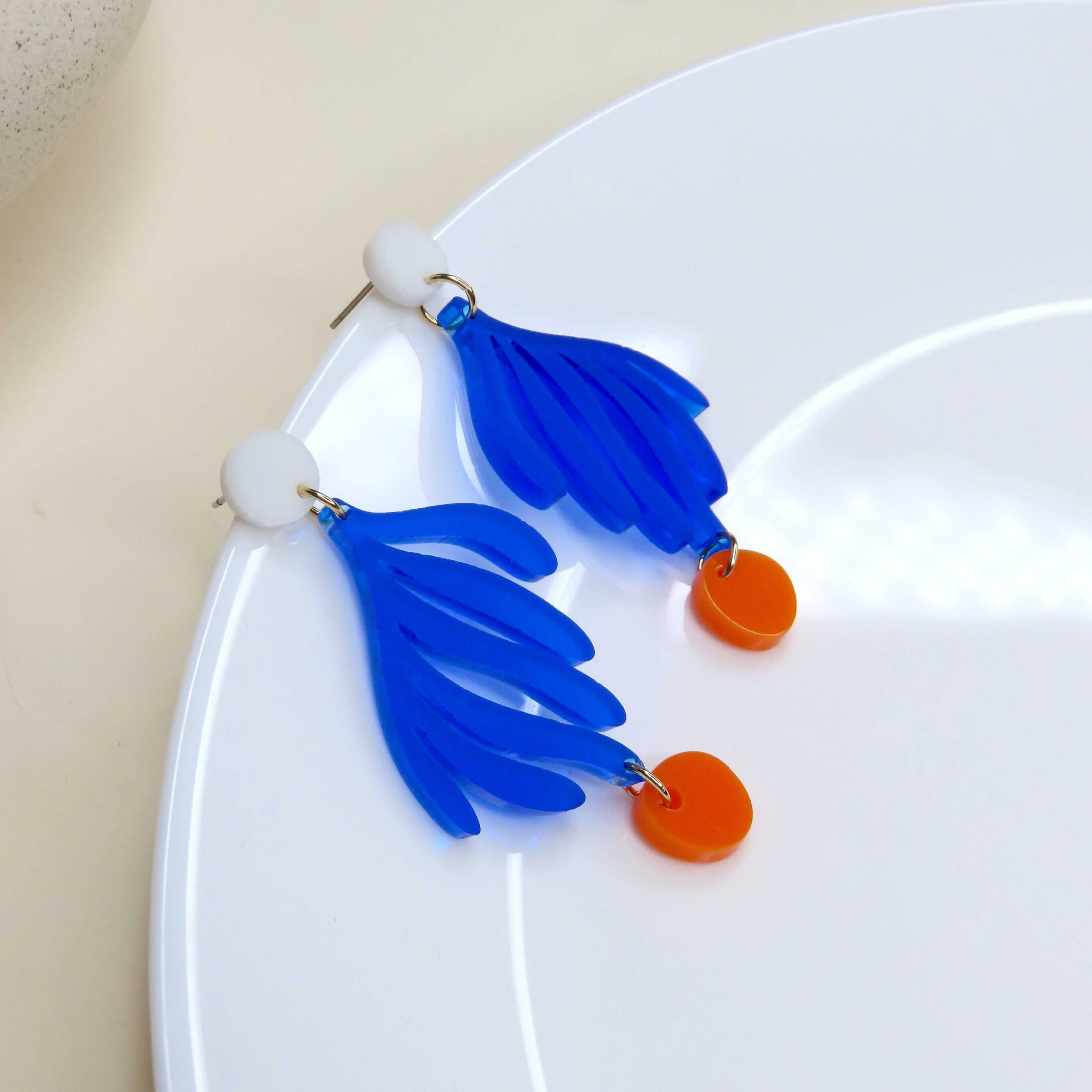 Auffällige Acryl-Ohrringe mit blauen, geschwungenen Blattmotiven und orangefarbenen Tropfen