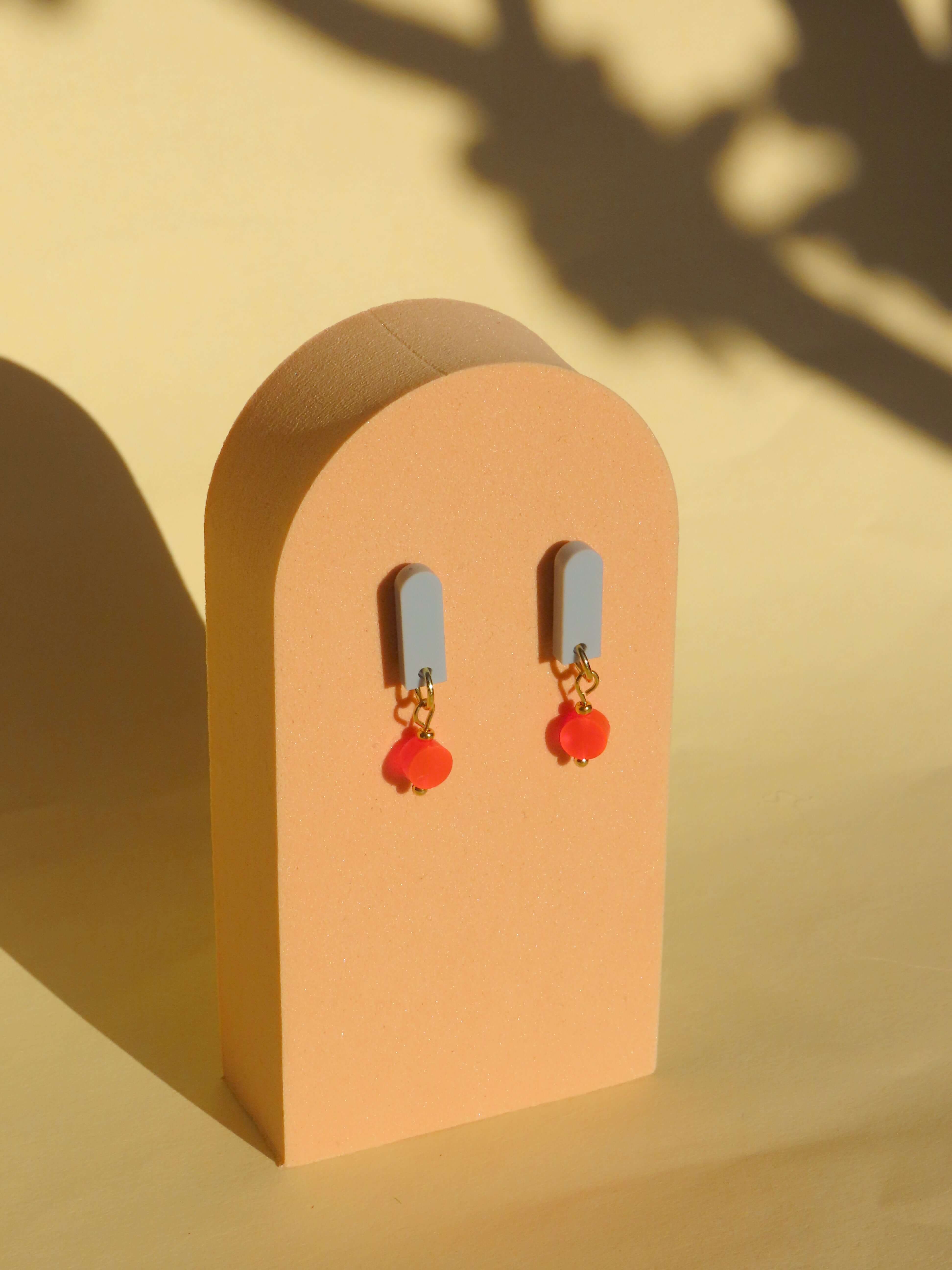 Handgemachte Salbei Neon Orange Paula Ohrringe aus Acryl und Edelstahl auf einem stilvollen Display.