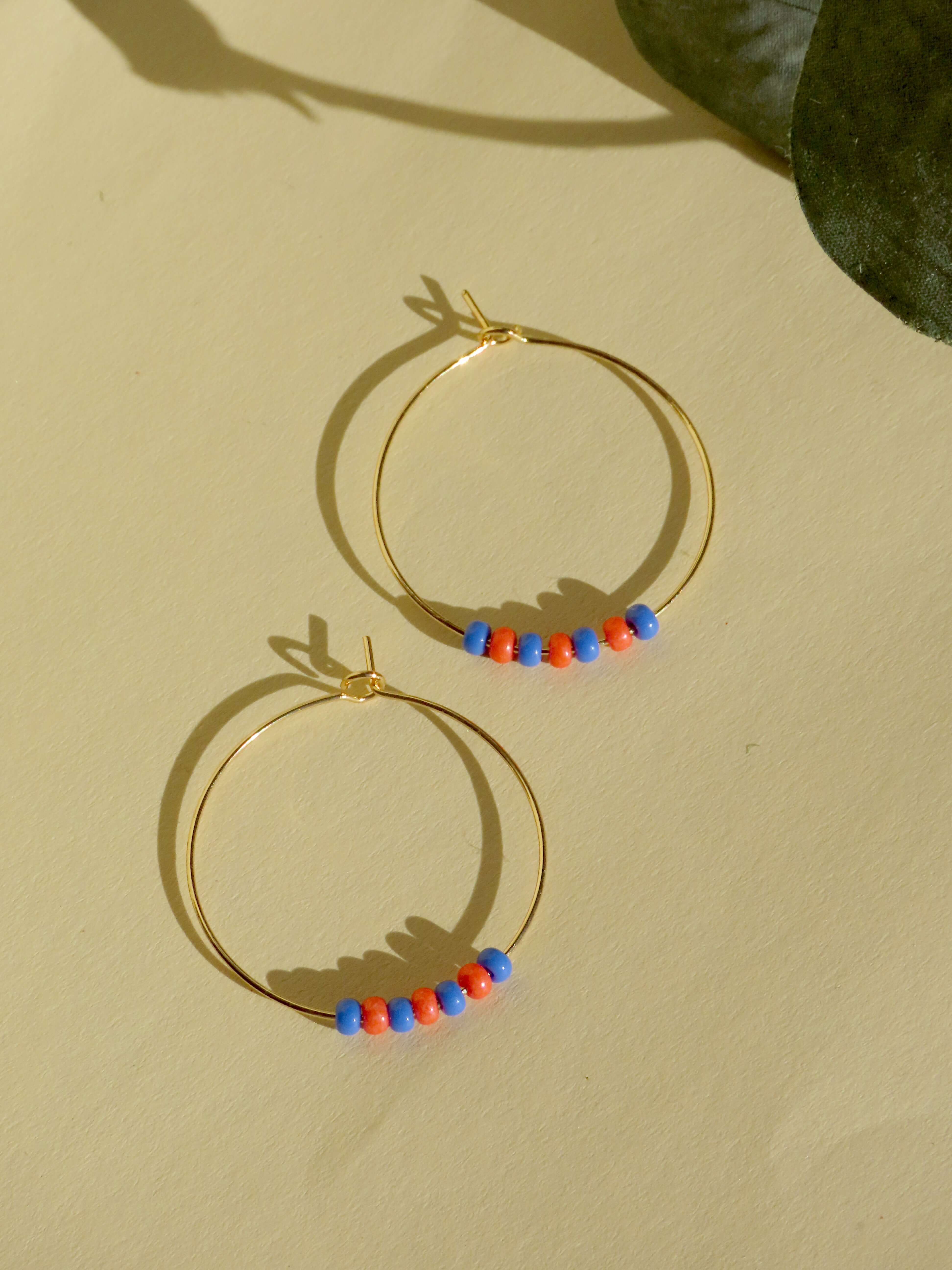Handcrafted gold-plated stainless steel hoops with blue and red Toho seed beads, lightweight and stylish.