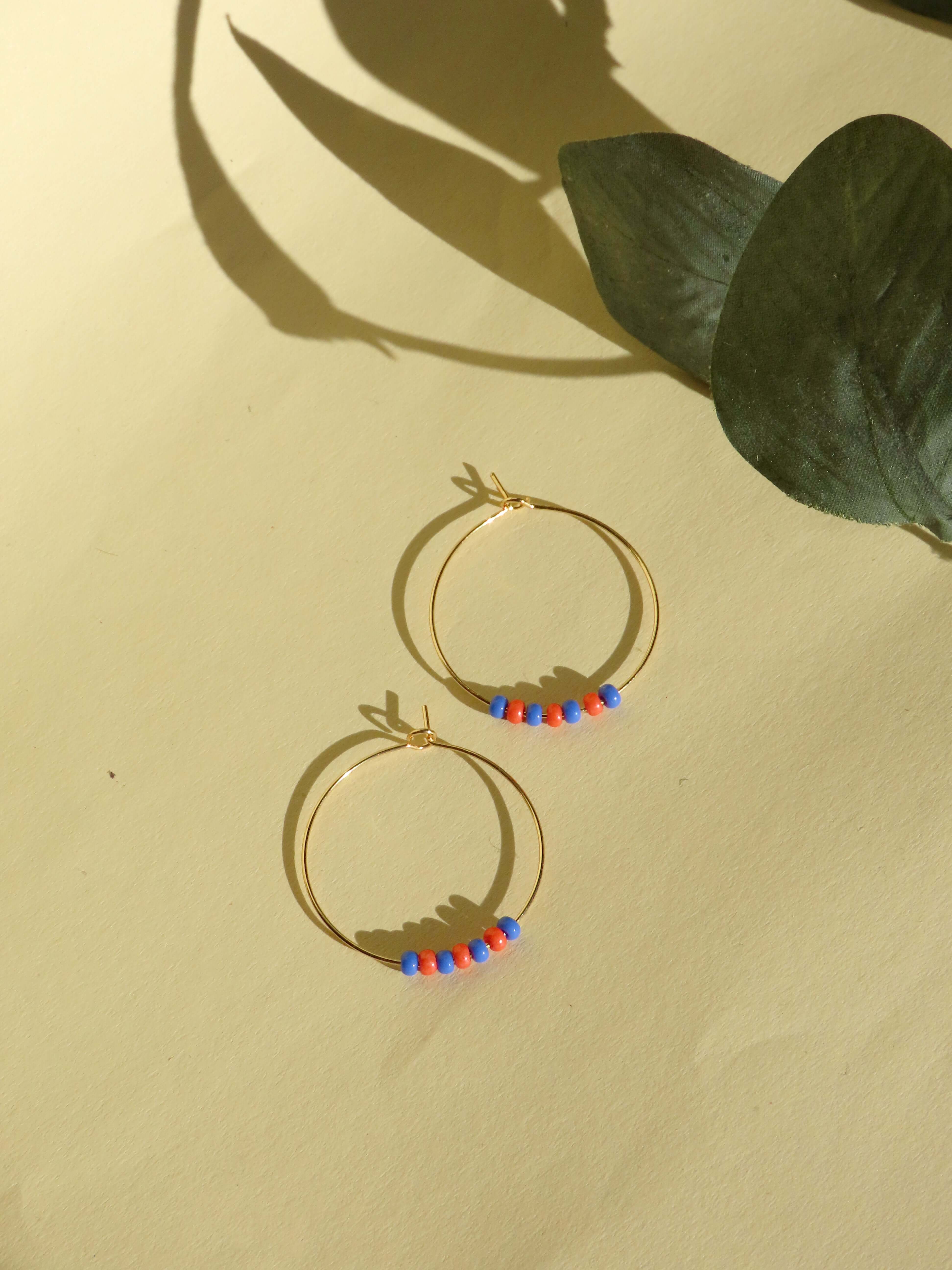 Handcrafted gold-plated stainless steel hoops with blue and red Toho seed beads, lightweight design, 3cm diameter.