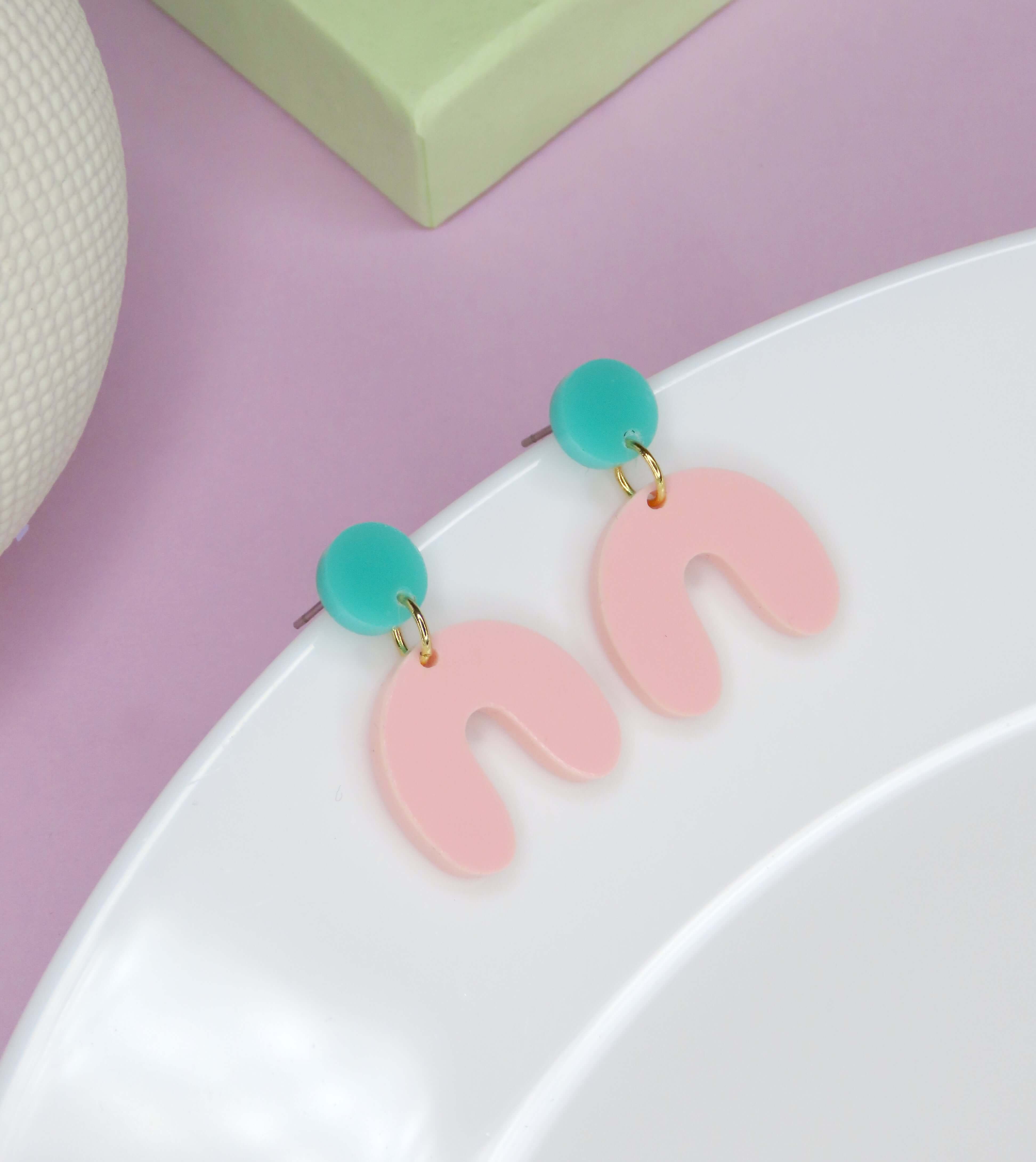 Handgemachte Ohrringe mit rundem türkisen Acrylstecker und rosa bogenförmigem Anhänger