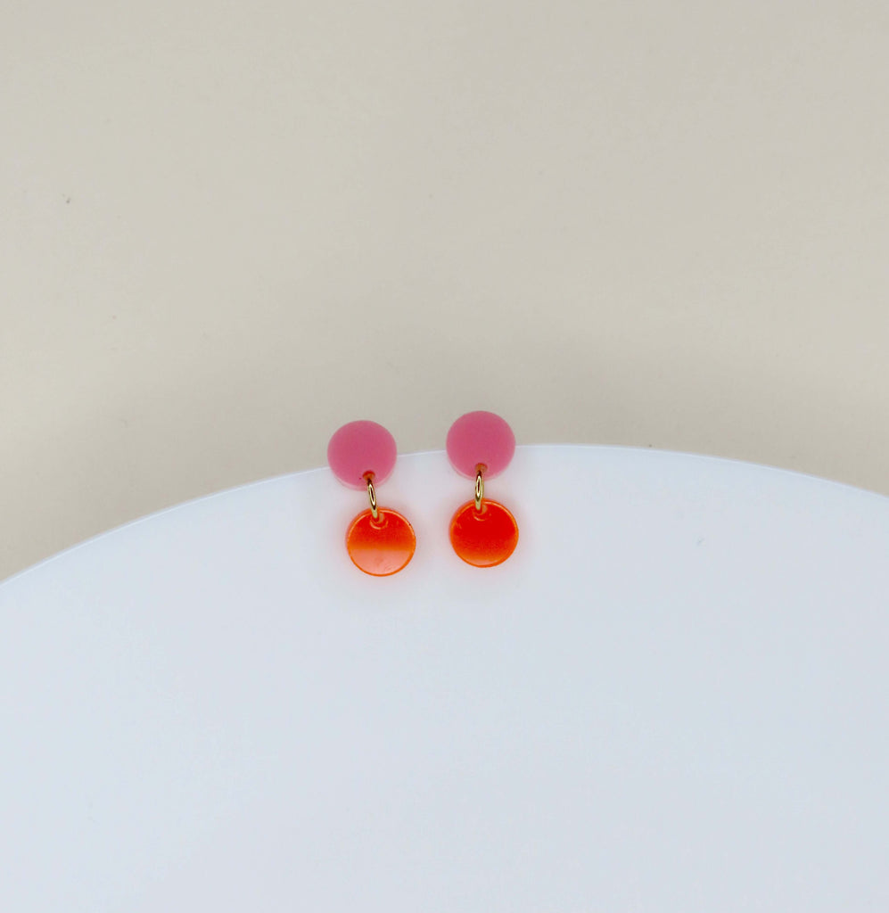zarte rosa acryl-stecker in kreisform mit abgesetztem neonorange-hänger und goldenem verbindungselement