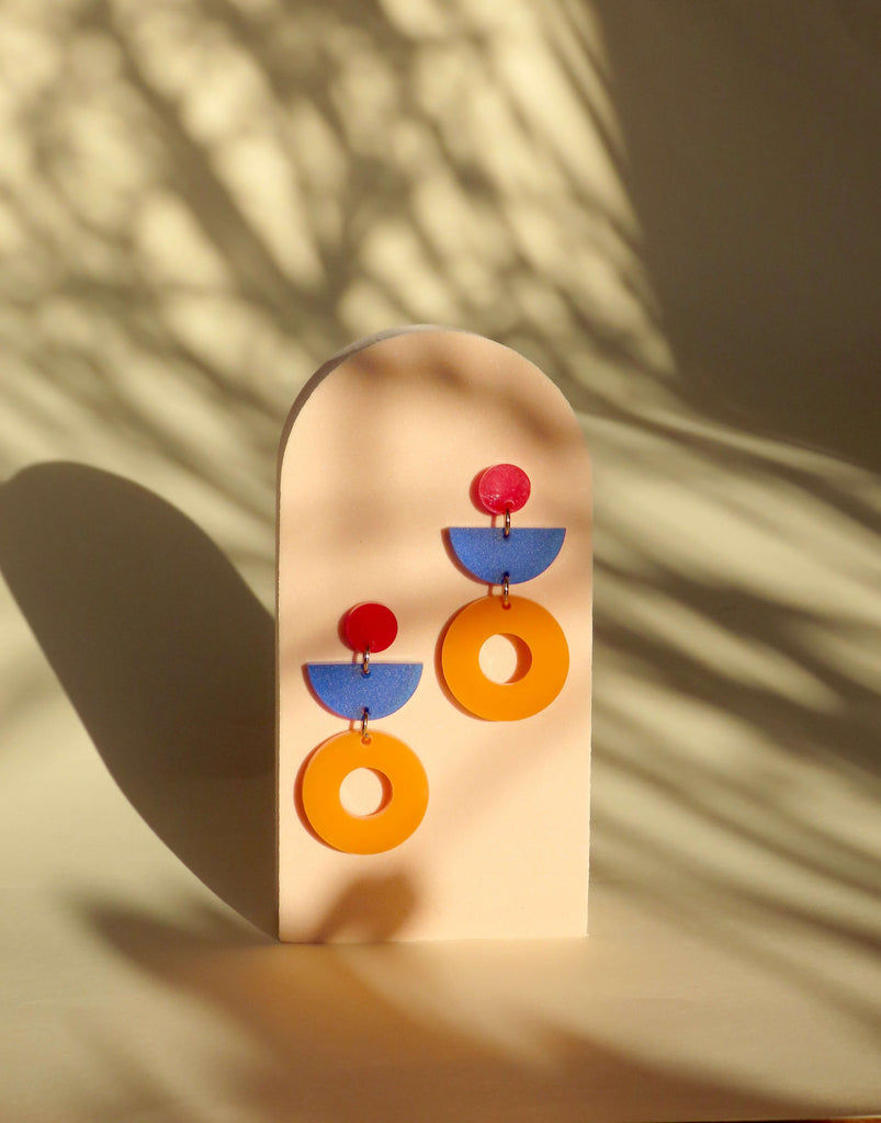 Geometrische Statement-Ohrringe aus Acryl mit orangefarbenen Ringen, blauen Halbkreisen und roten Punkten, kombiniert zu einem farbenfrohen Design