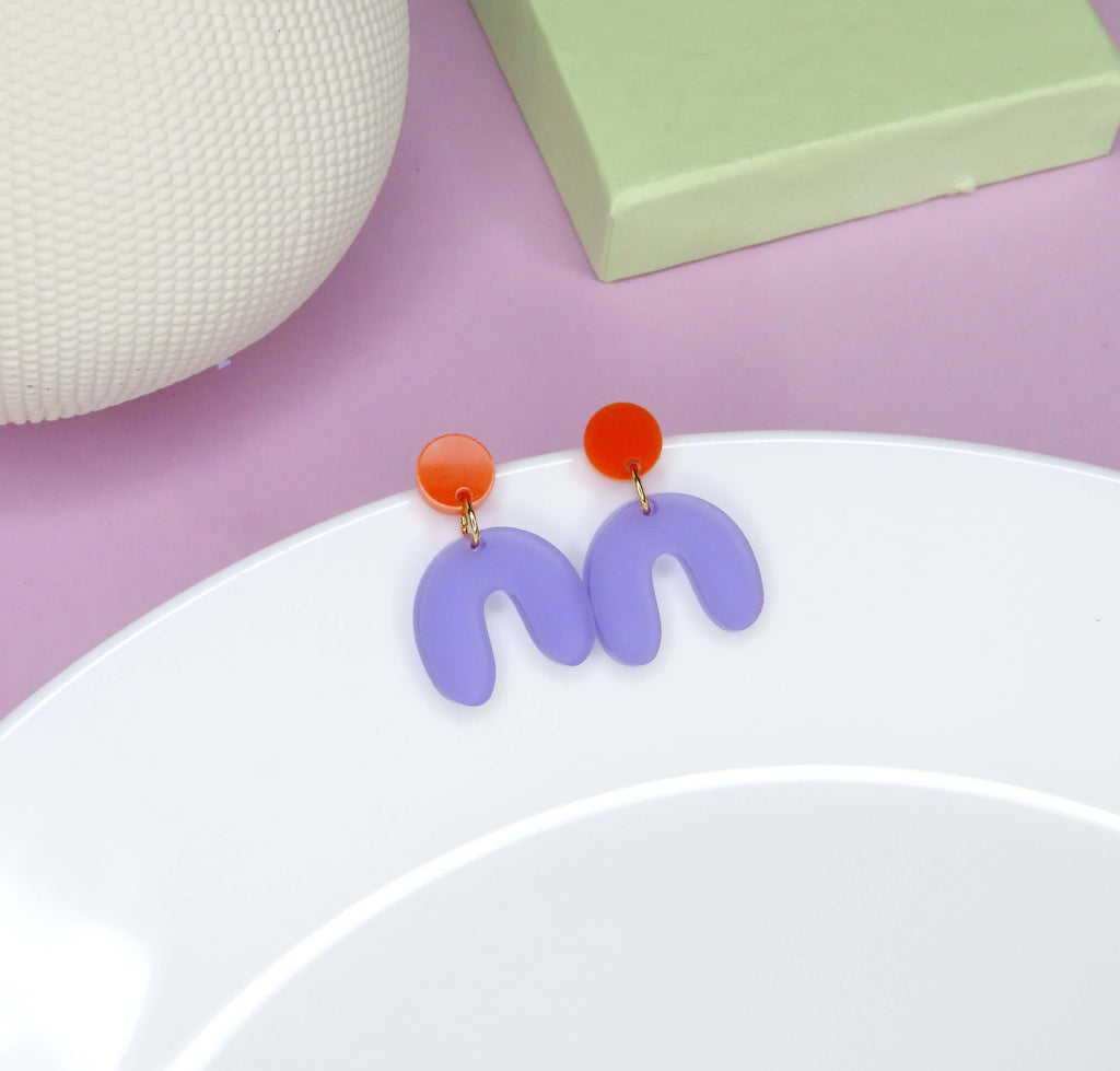 Ohrstecker aus Acryl mit rundem Element in kräftigem Orange und bogenförmigem Anhänger in transparentem Lila