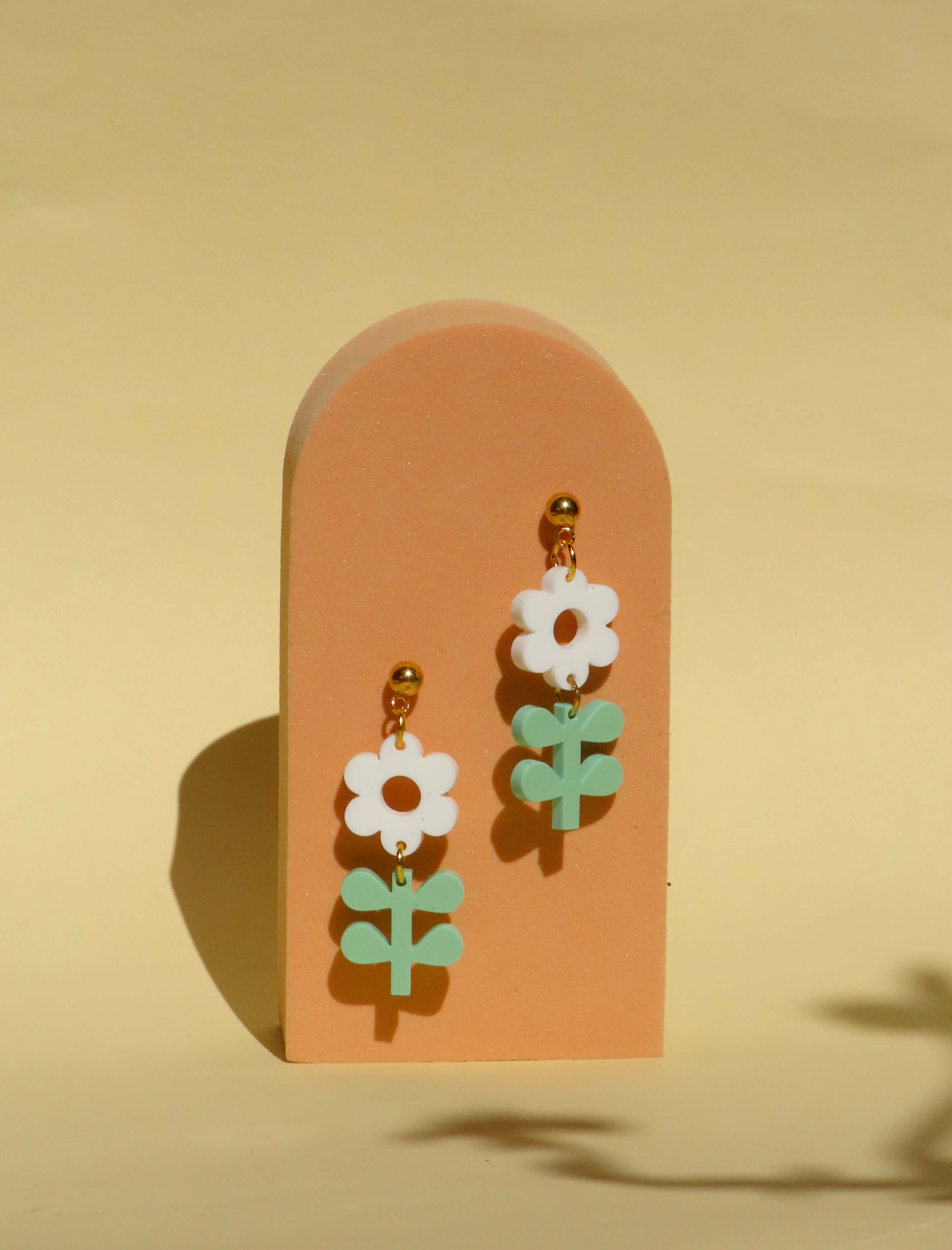 Florale Ohrringe mit weißer Blüte und mint grünen Blättern an goldenen Edelstahlsteckern.