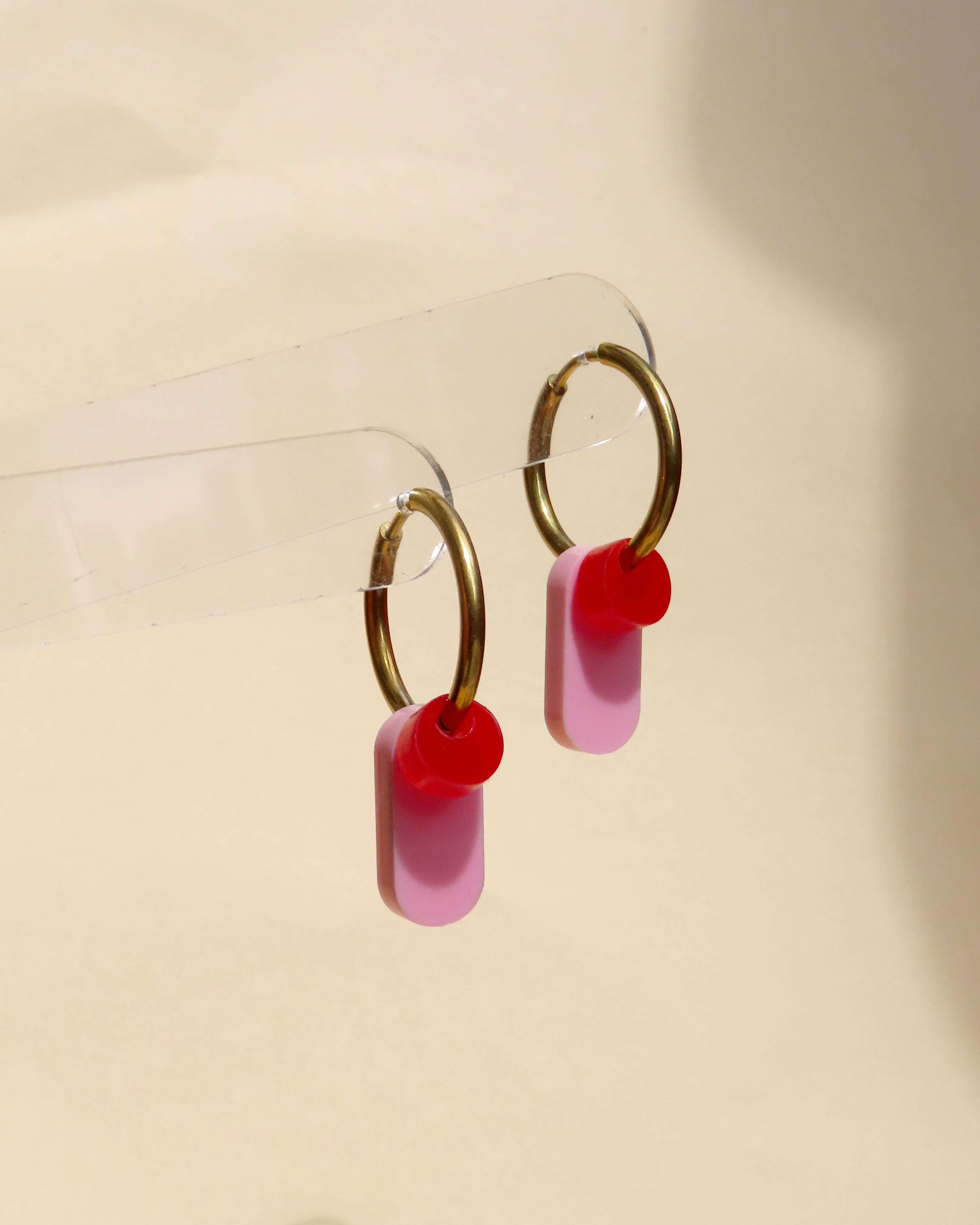 Modern designte Ohrringe mit goldfarbenem Ring und zweifarbigen Acrylanhängern in Rot und Rosa