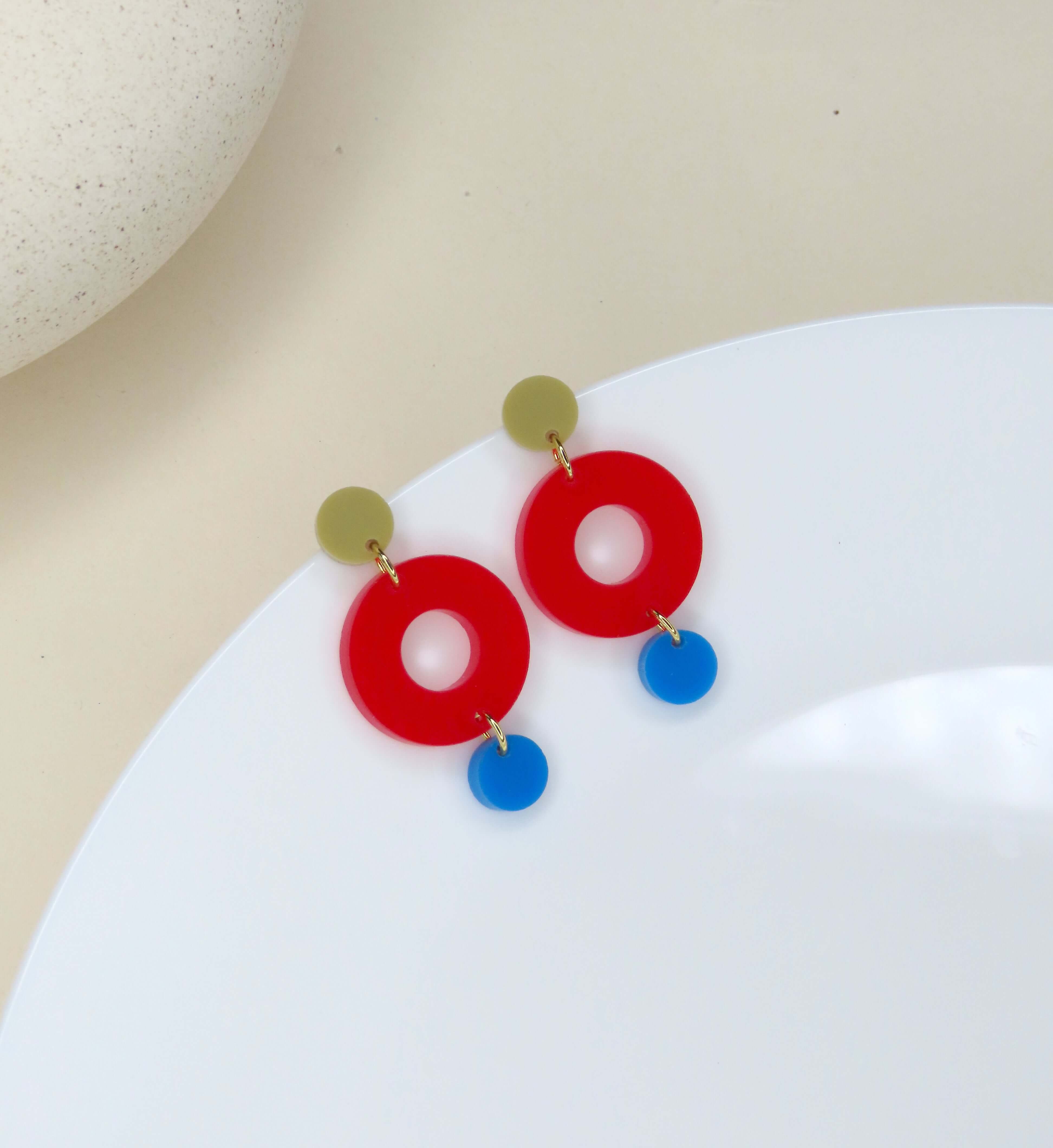 Kreisförmige Ohrstecker aus Acryl mit offener Mitte in Rot, ergänzt durch sandfarbenen und blauen Kreis