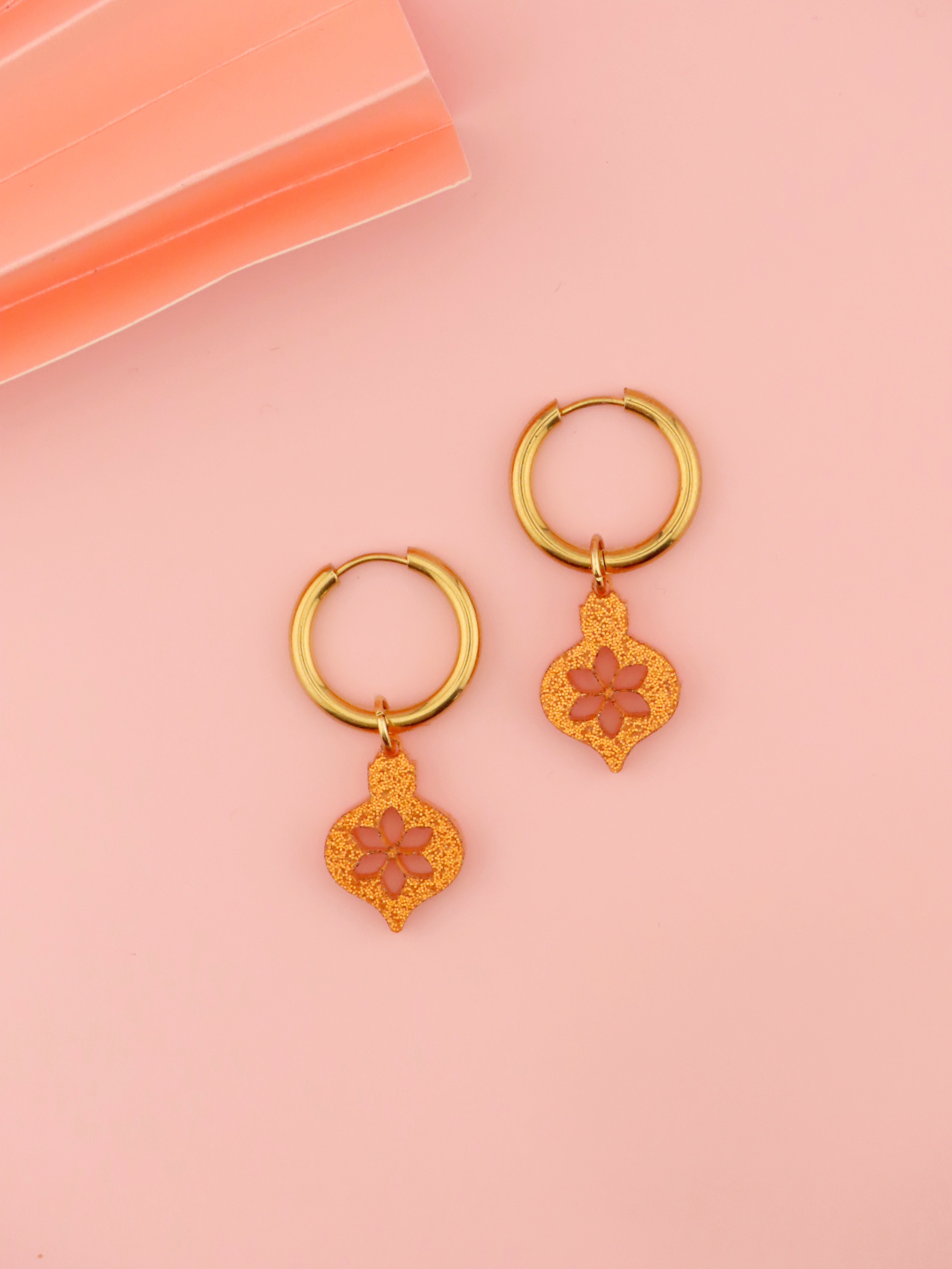 vergoldete edelstahlcreolen mit warm orangefarbenen acrylanhängern in ornamentform mit feinem glitterglanz