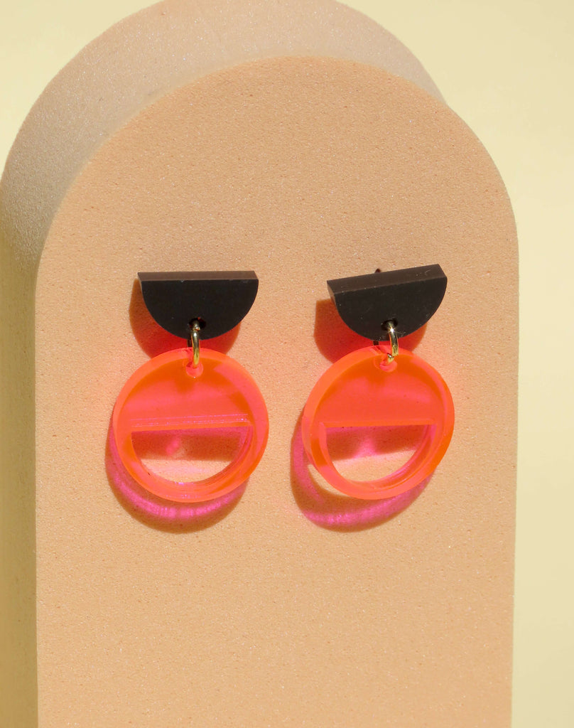 Grafische Ohrstecker aus Acryl, bestehend aus schwarzem Halbkreis und transparent leuchtendem Neon-Orange Kreis, Kontrastdesign