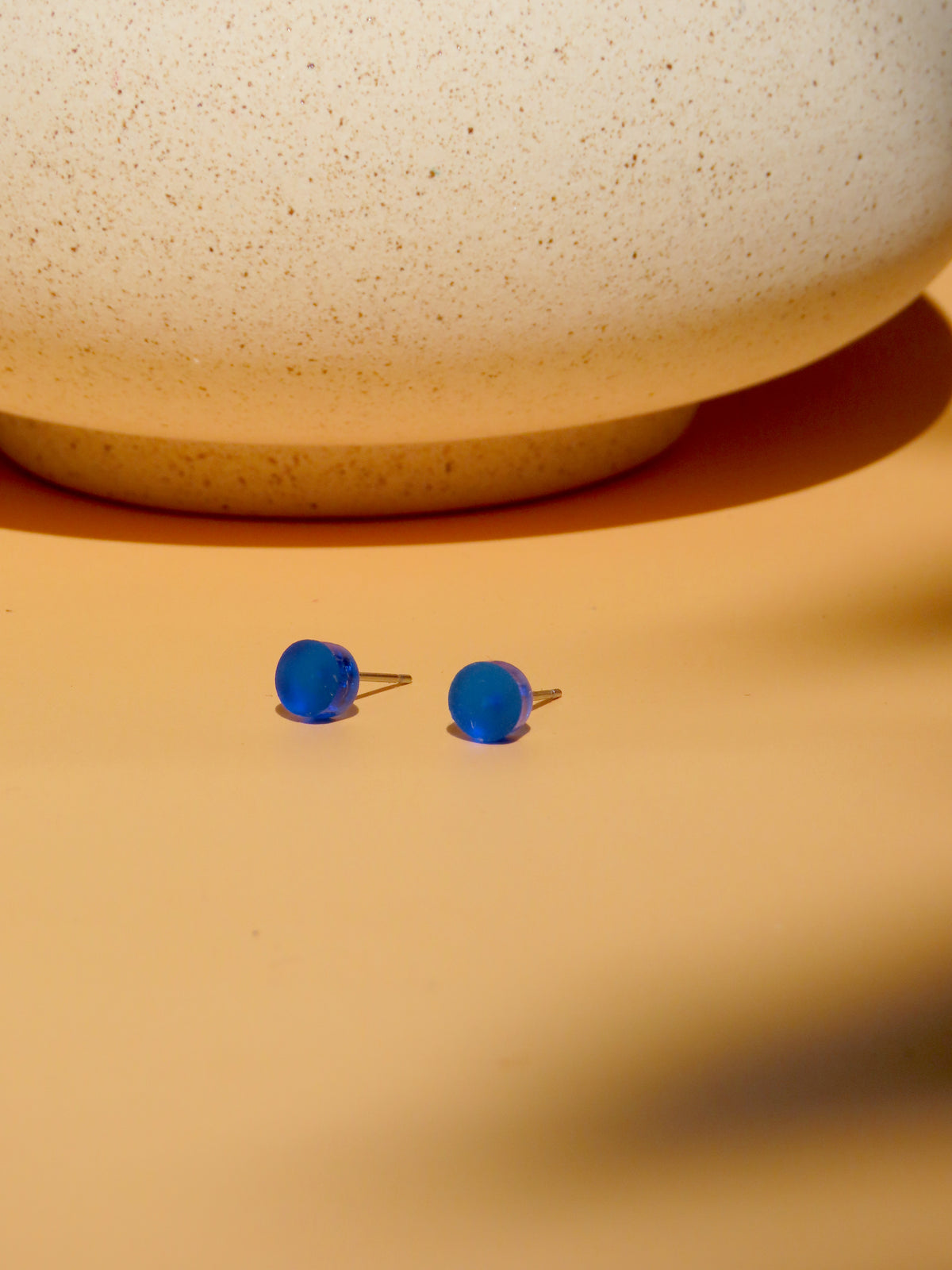 Zwei runde, tintenblaue Ink Pop Ohrstecker mit Acrylscheiben auf apricotfarbenem Untergrund, von vorne fotografiert.
