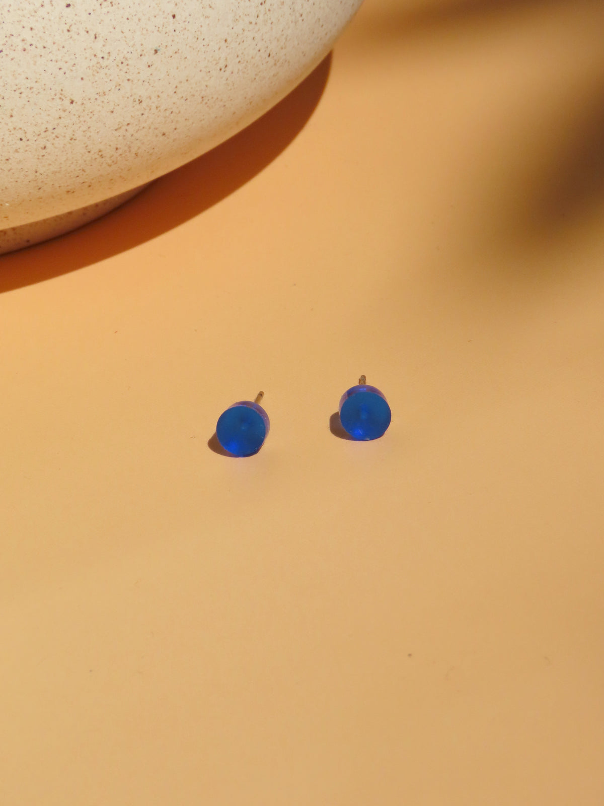 laue Ink Pop Ohrstecker aus Acryl und Edelstahl in Schrägansicht mit sichtbaren Steckerstiften auf apricotfarbenem Untergrund