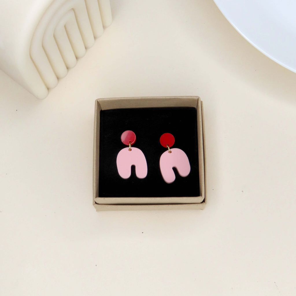Geometrische Ohrringe in Rot und Rosa, bestehend aus rundem Kreisstecker und verspieltem Bogenanhänger