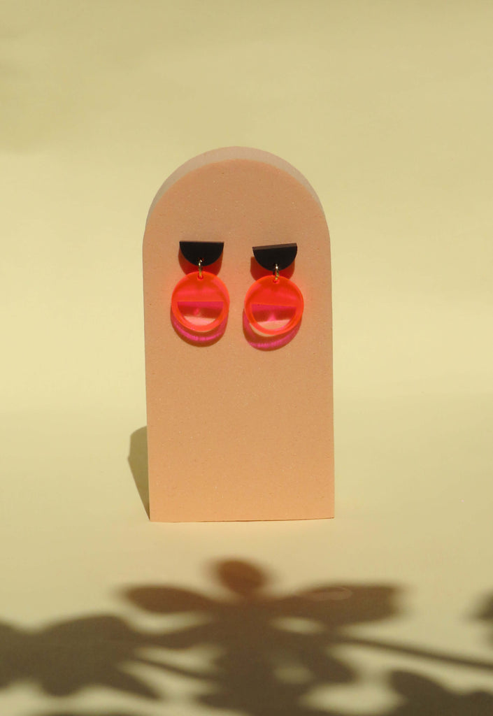 Geometrische Ohrstecker aus Acryl mit schwarzem Halbkreis und transparentem Neon-Pink Kreis, kombiniert mit Edelstahlstecker