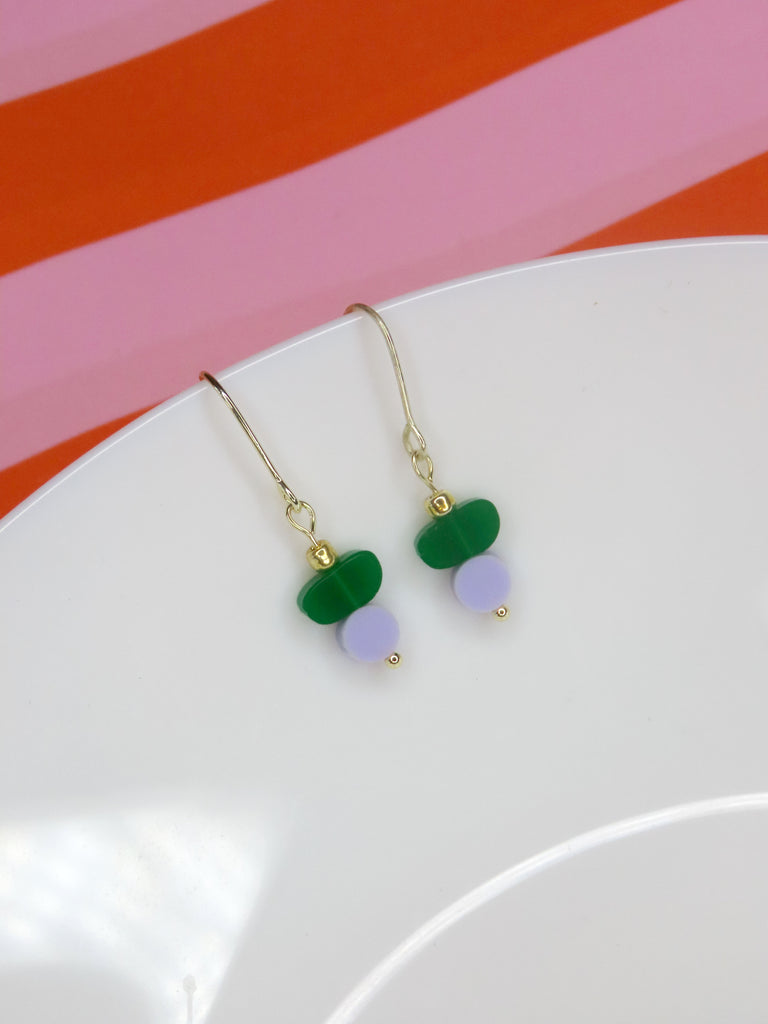 Zarte Hakenohrringe mit grünem und lila Acryl sowie goldfarbenem Detail – handgemachter Modeschmuck.