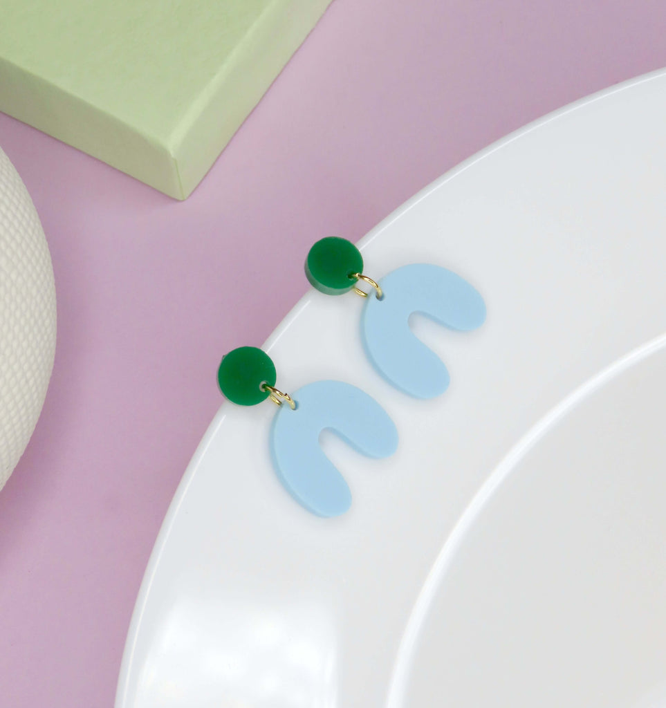 Minimalistischer Statement-Ohrring mit hellblauem Acrylbogen und grünem Kreis auf Edelstahlstecker