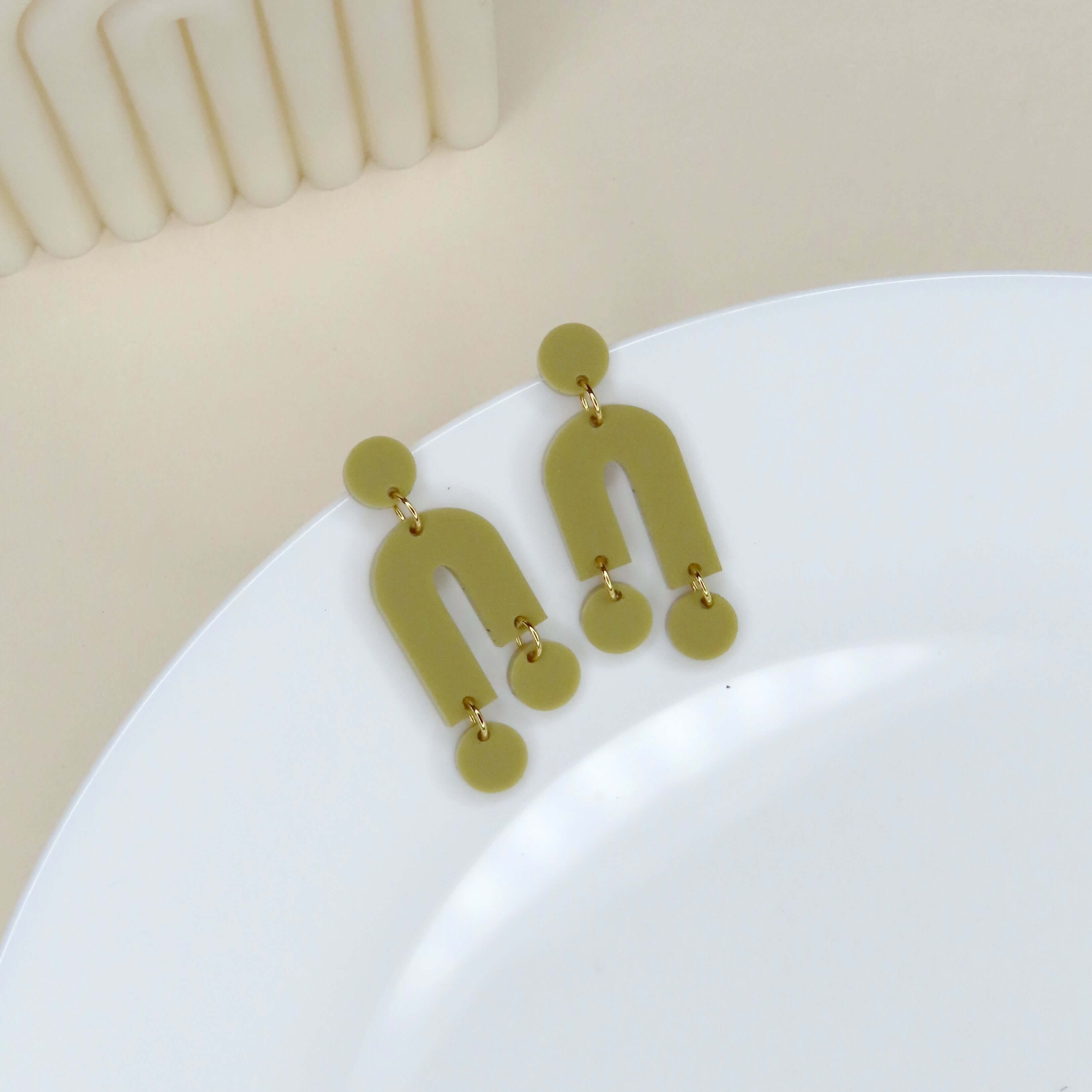 Asymmetrische Mismatch Ohrringe aus sandfarbenem Acryl mit offenem Bogen und kleinen runden Elementen, verbunden durch goldene Ringe