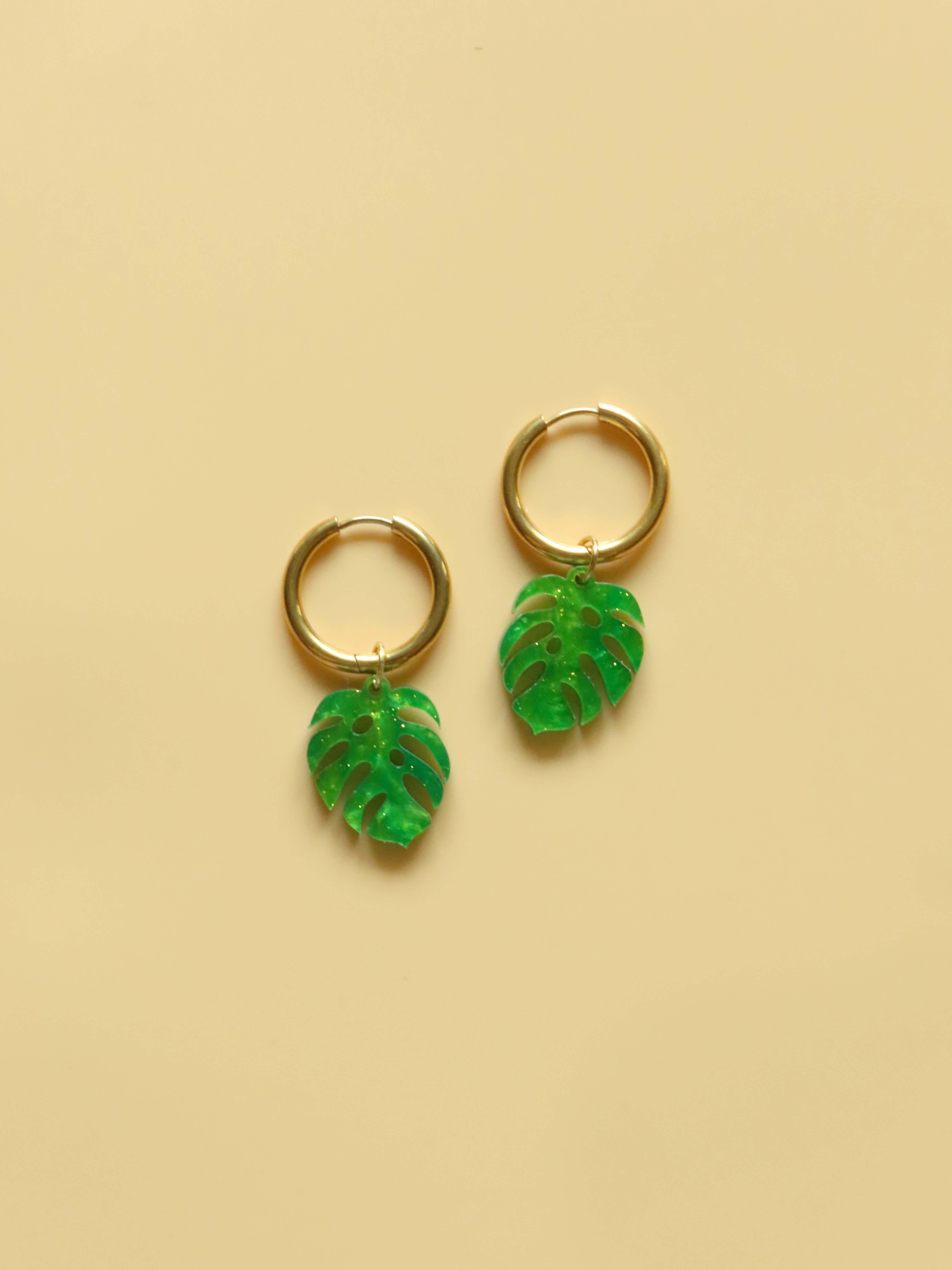 Monstera Creolen mit grün gemusterten Acrylblättern und feinen goldenen Glitzerpartikeln an vergoldeten Edelstahlringen