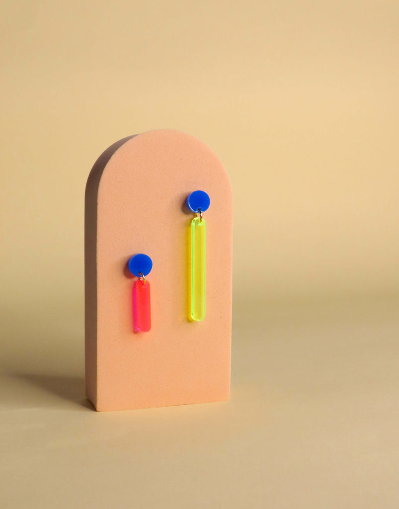 Auffällige Acryl-Ohrringe in asymmetrischer Form mit Neonpinkem und Neongelbem Anhänger an blauen Edelstahlsteckern