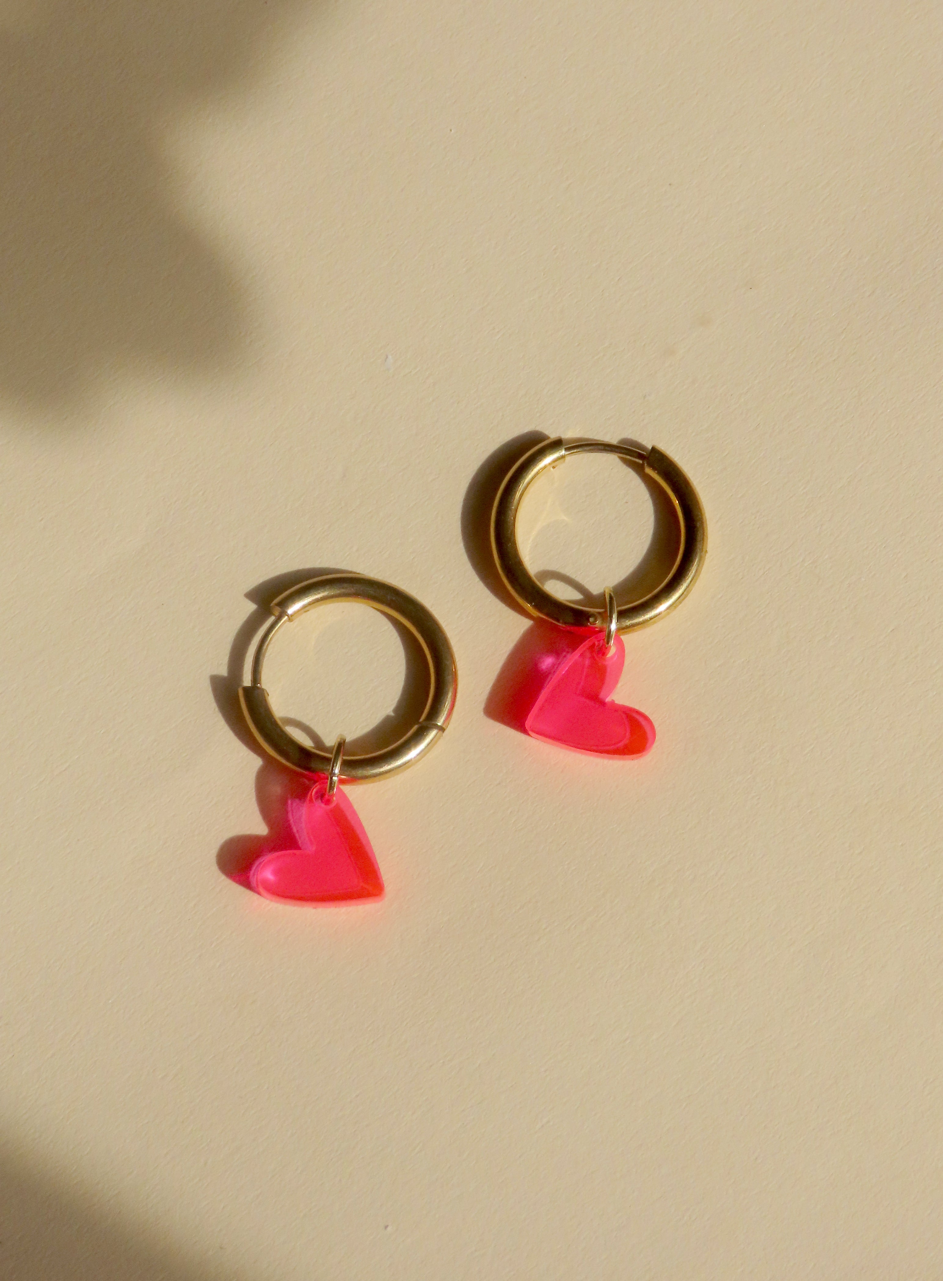 Verspielte Creolen mit transparenten Herzanhängern in Neon Pink und goldglänzendem Edelstahl