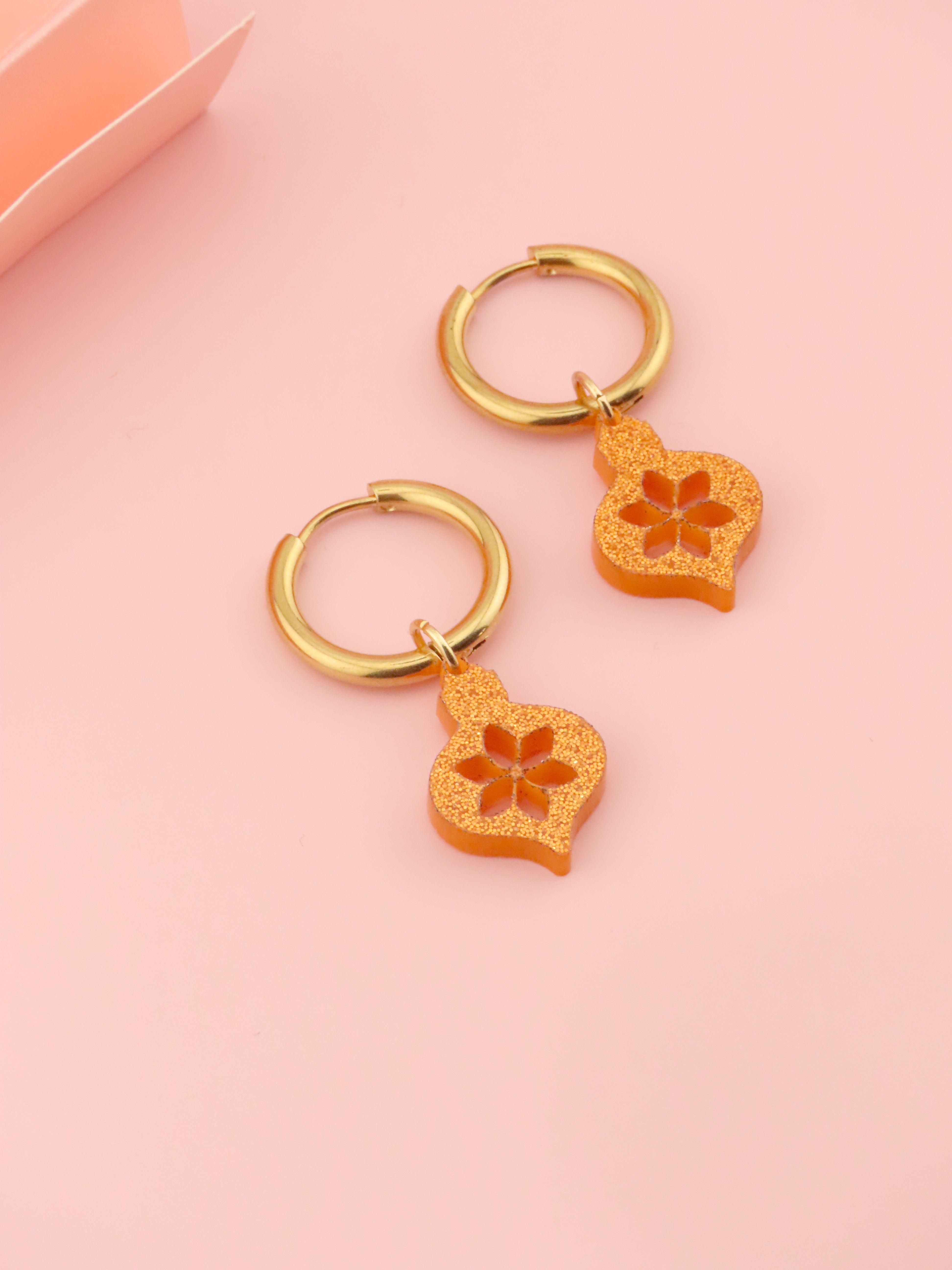 goldene creolen mit orangeglitzernden acrylornamenten in floral ausgeschnittener form