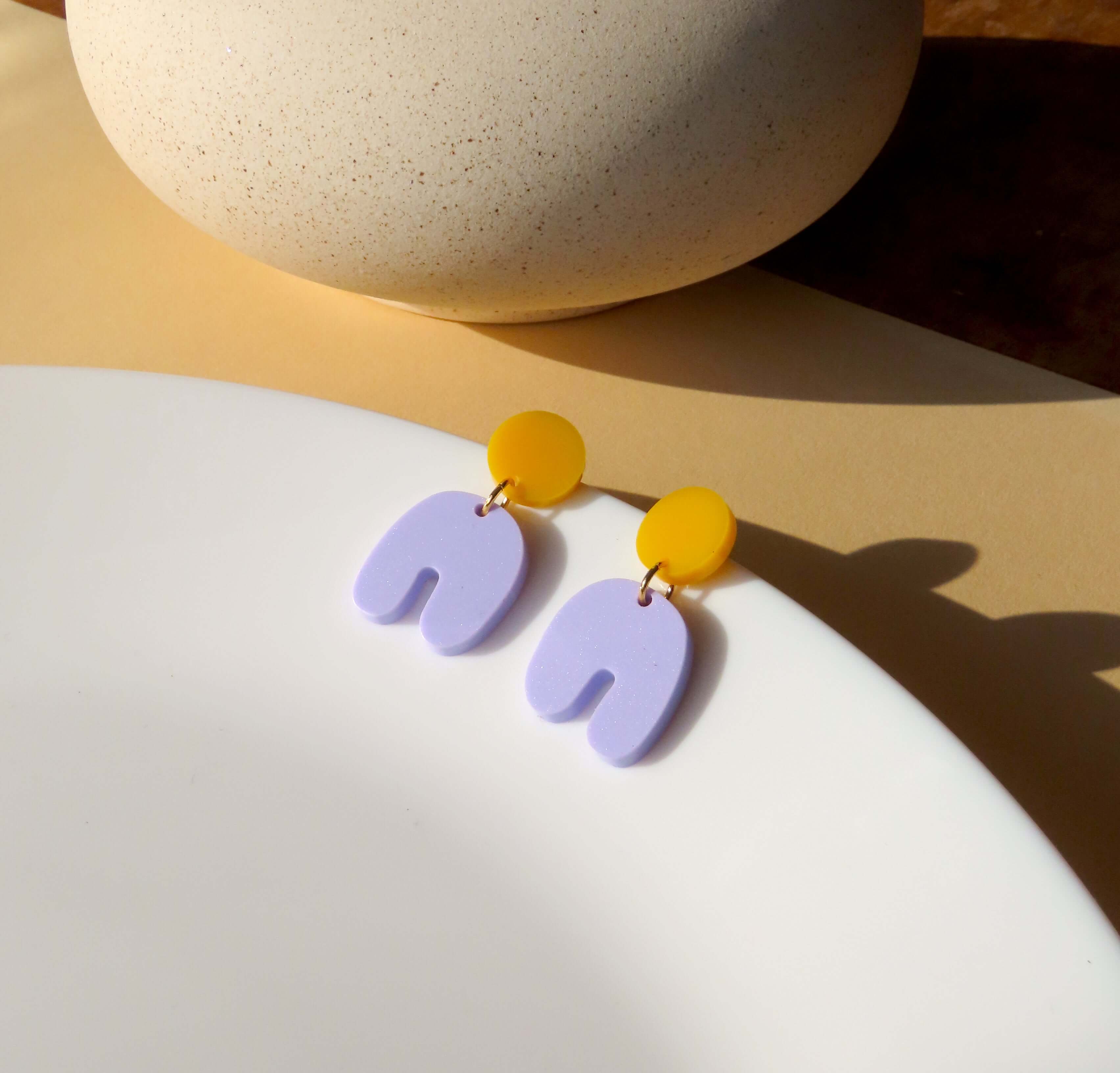 Acryl Ohrringe in Goldgelb und Flieder mit rundem Stecker und geschwungenem Bogenanhänger in asymmetrischer Form