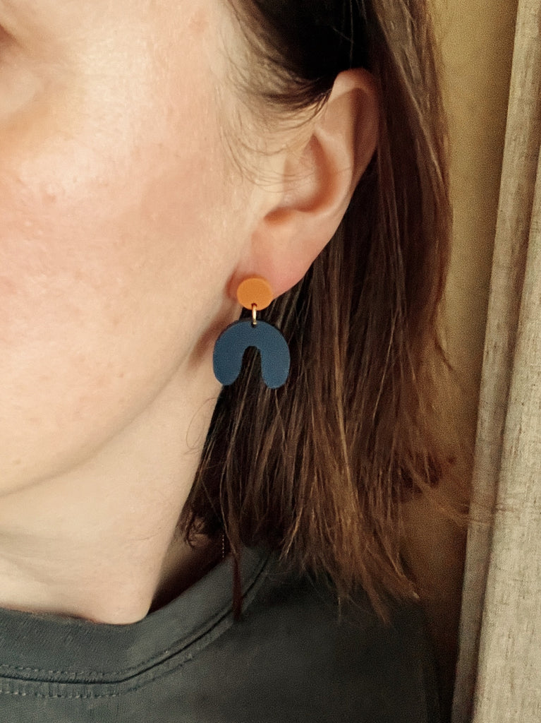 kleine moderne acryl‑ohrringe in arch‑form mit warmem terracotta‑stecker und dunkelblauem anhänger