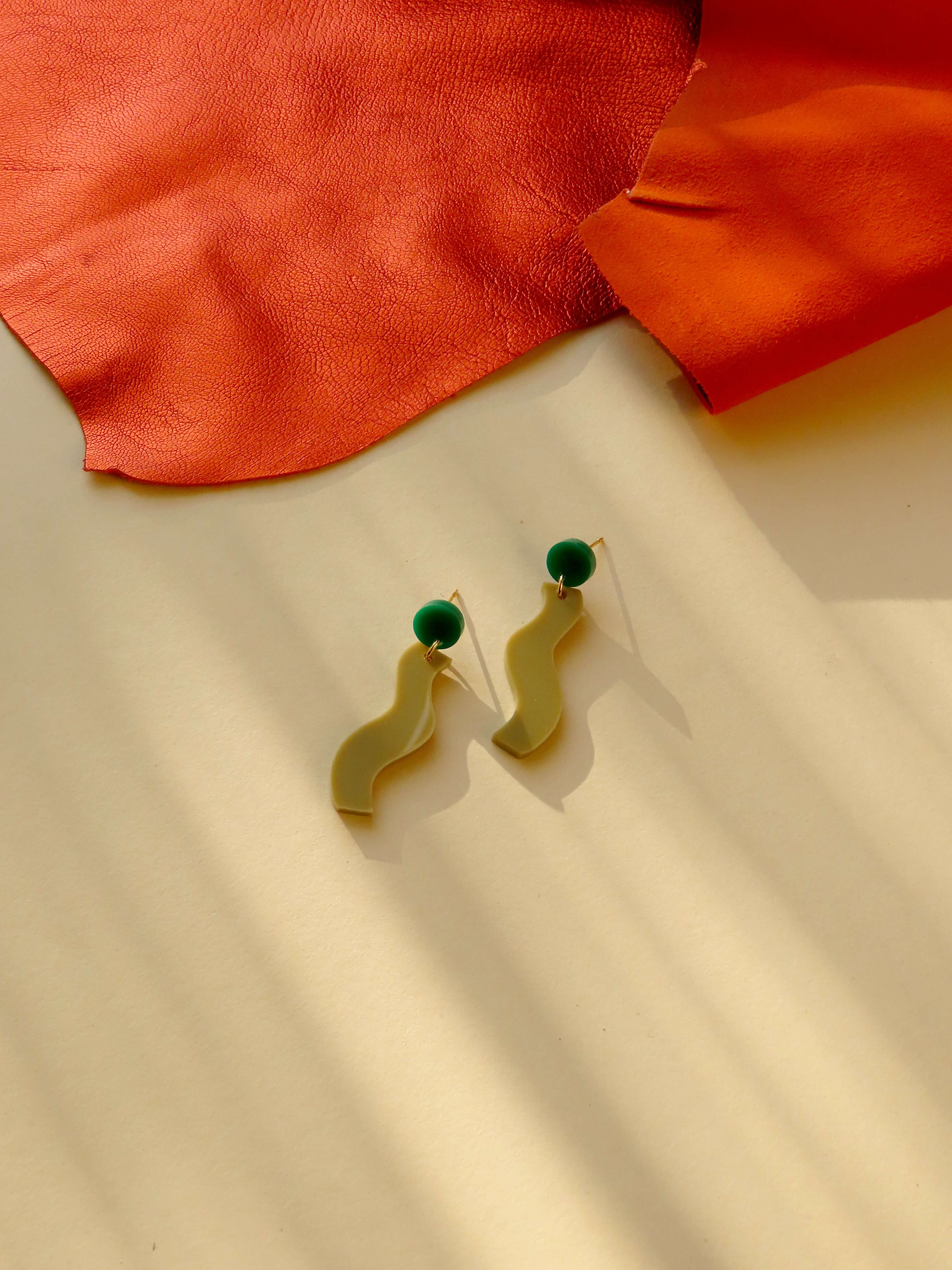 Acrylohrringe mit rundem grünem Stecker und geschwungenem beigefarbenem Anhänger in Wellenform