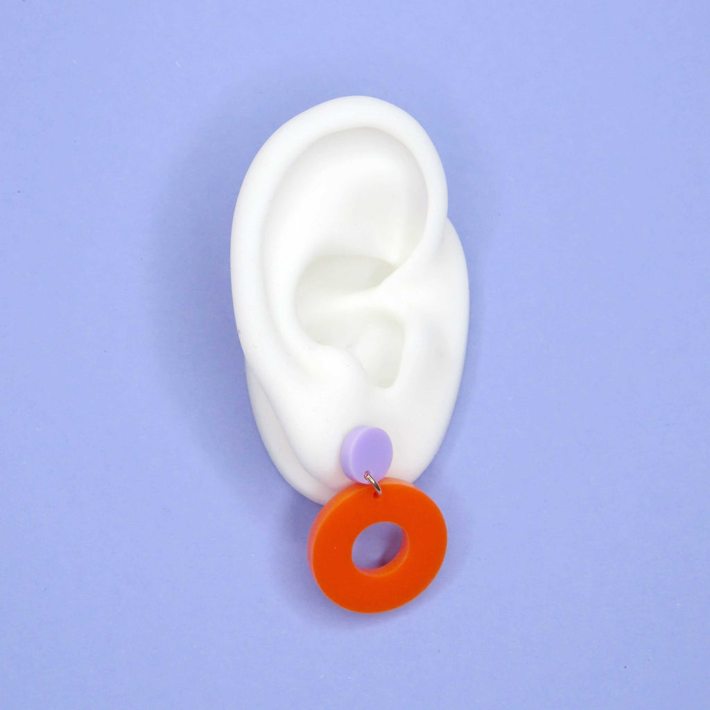 Kreisförmige Ohrstecker aus Acryl in Flieder mit anhängendem orangem Ringdesign und Edelstahlstecker