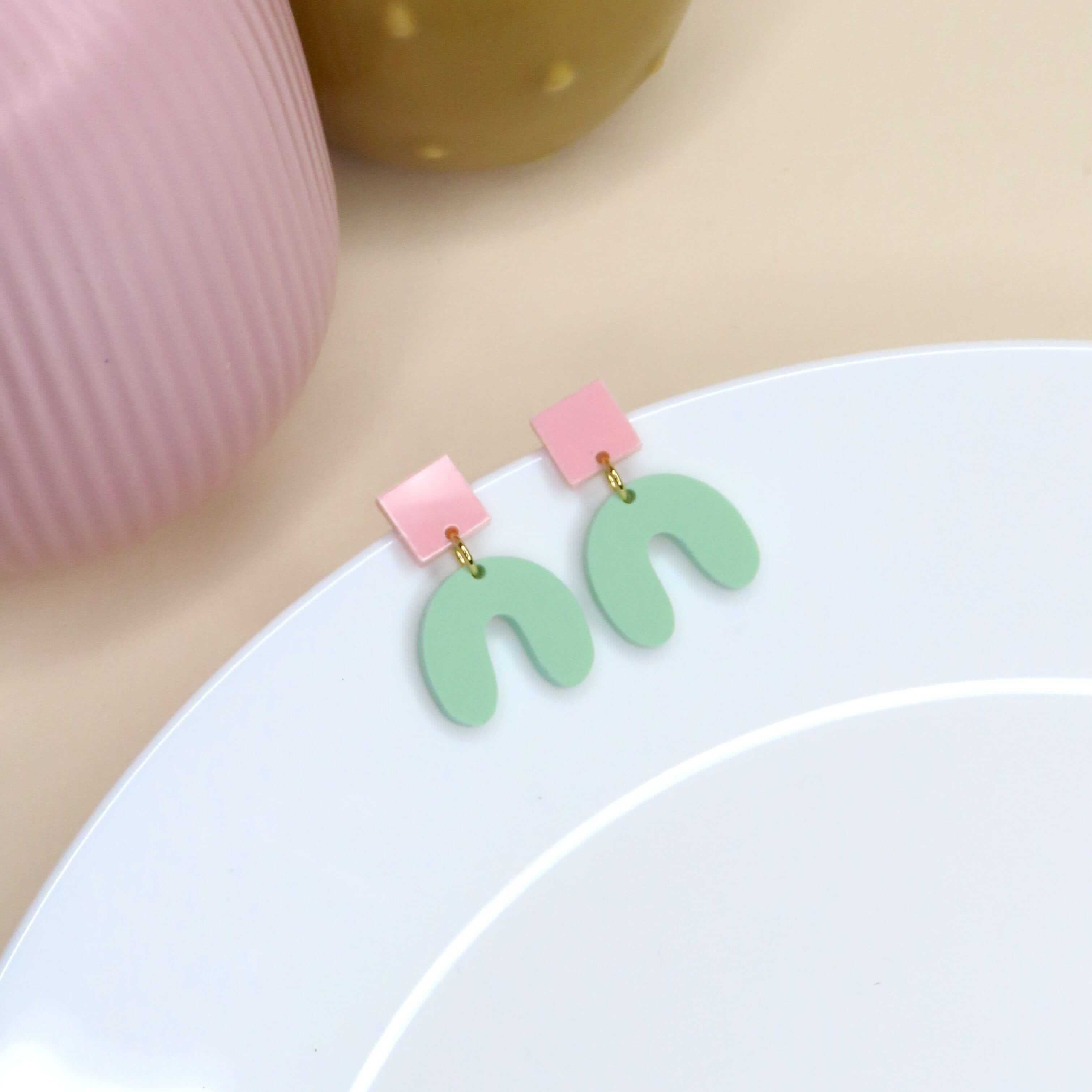 Handgefertigte Acrylohrringe mit rosa Quadrat-Stecker und mintgrünem Bogenanhänger in offener Hufeisenform